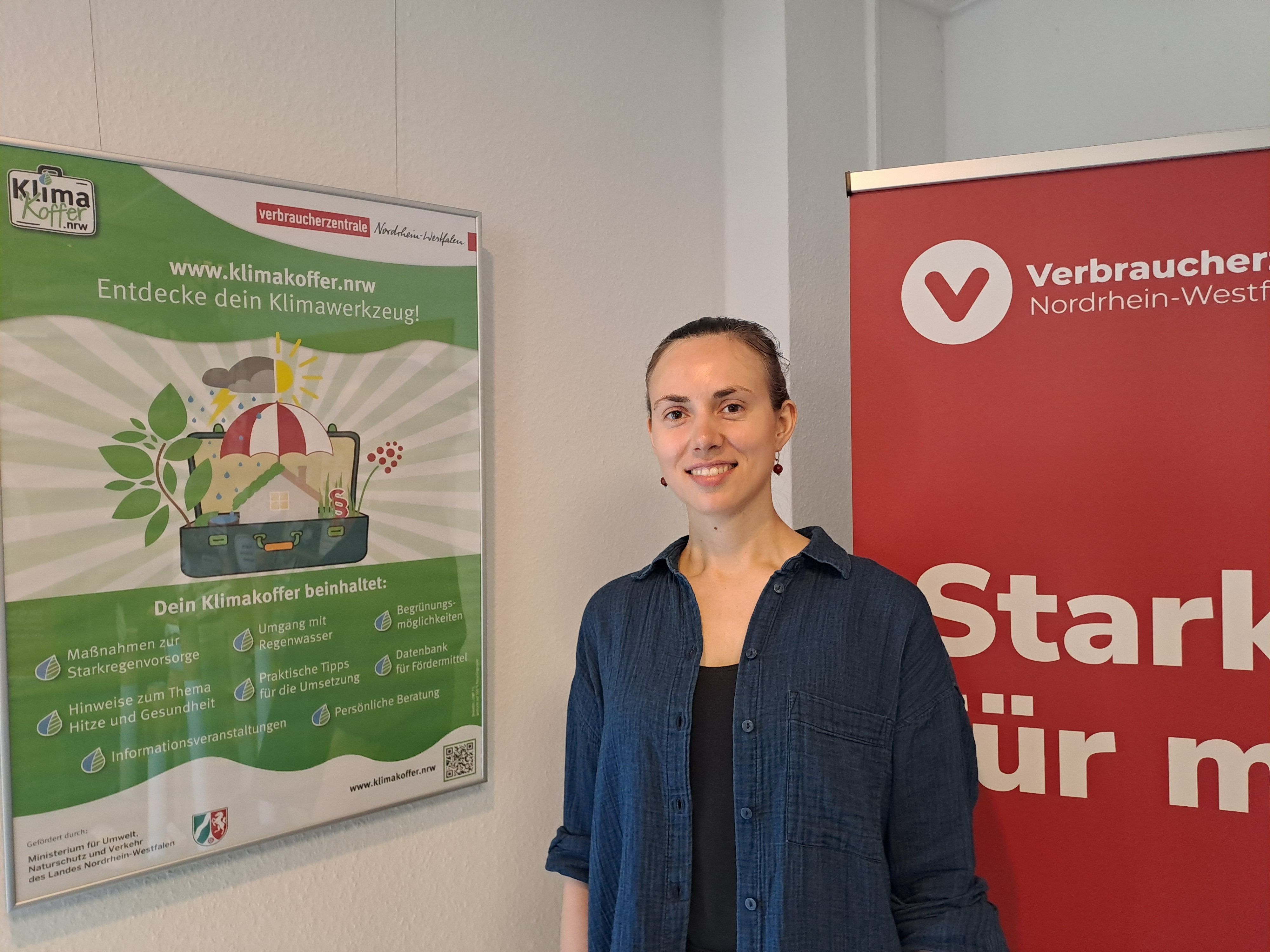 Eine Frau steht vor Plakaten und lächelt.