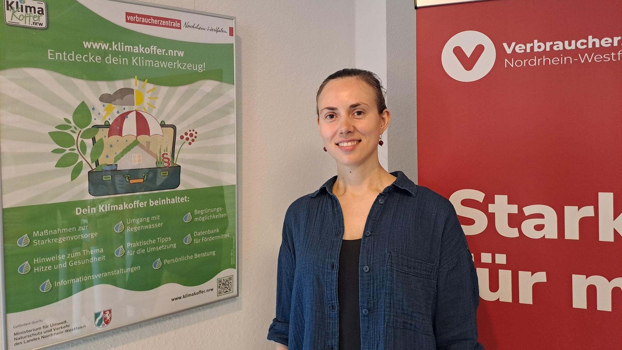 Eine Frau steht vor Plakaten und lächelt.