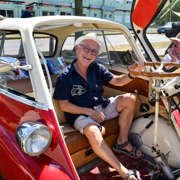 Zu sehen ist ein Mann, der in einer offenen Isetta sitzt, einem Oldtimer-Auto.