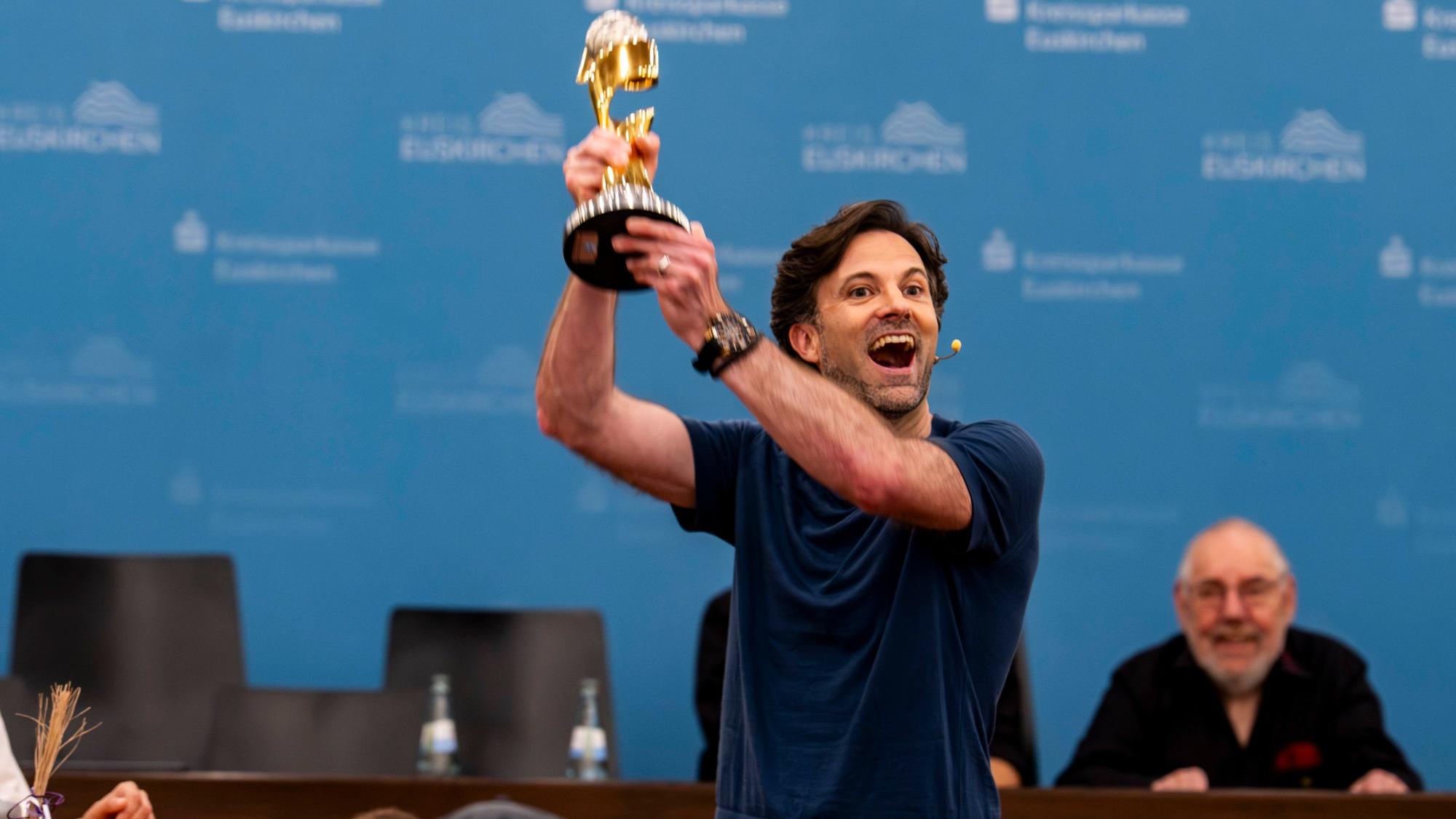 Das Bild zeigt Sebastian Tittelbach, der den Weltmeisterpokal in die Höhe reckt.