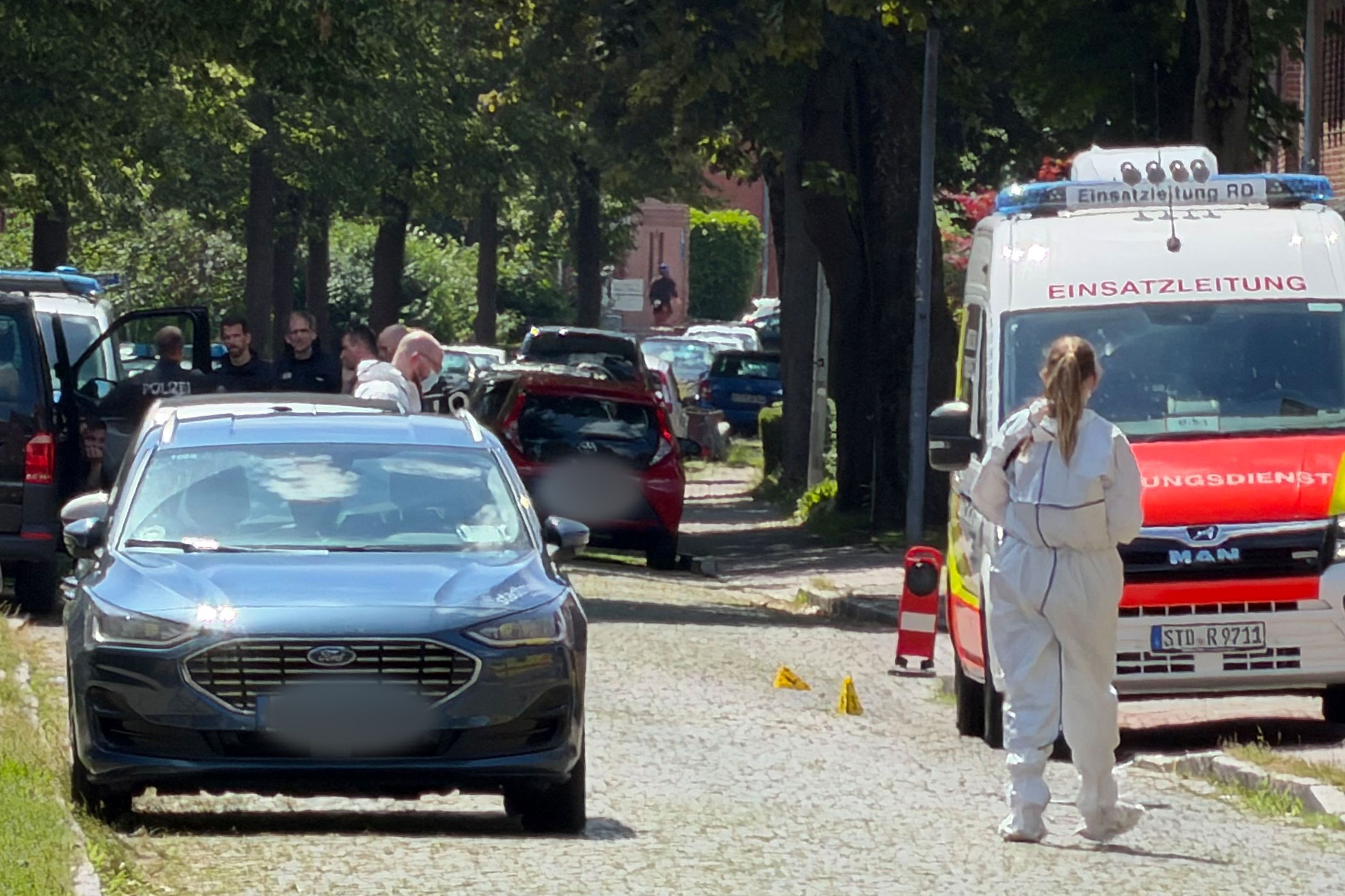 Einsatzkräfte und die Spurensicherung stehen auf einer Straße in Stade. Hier sind fünf Menschen durch Schüsse gestorben.