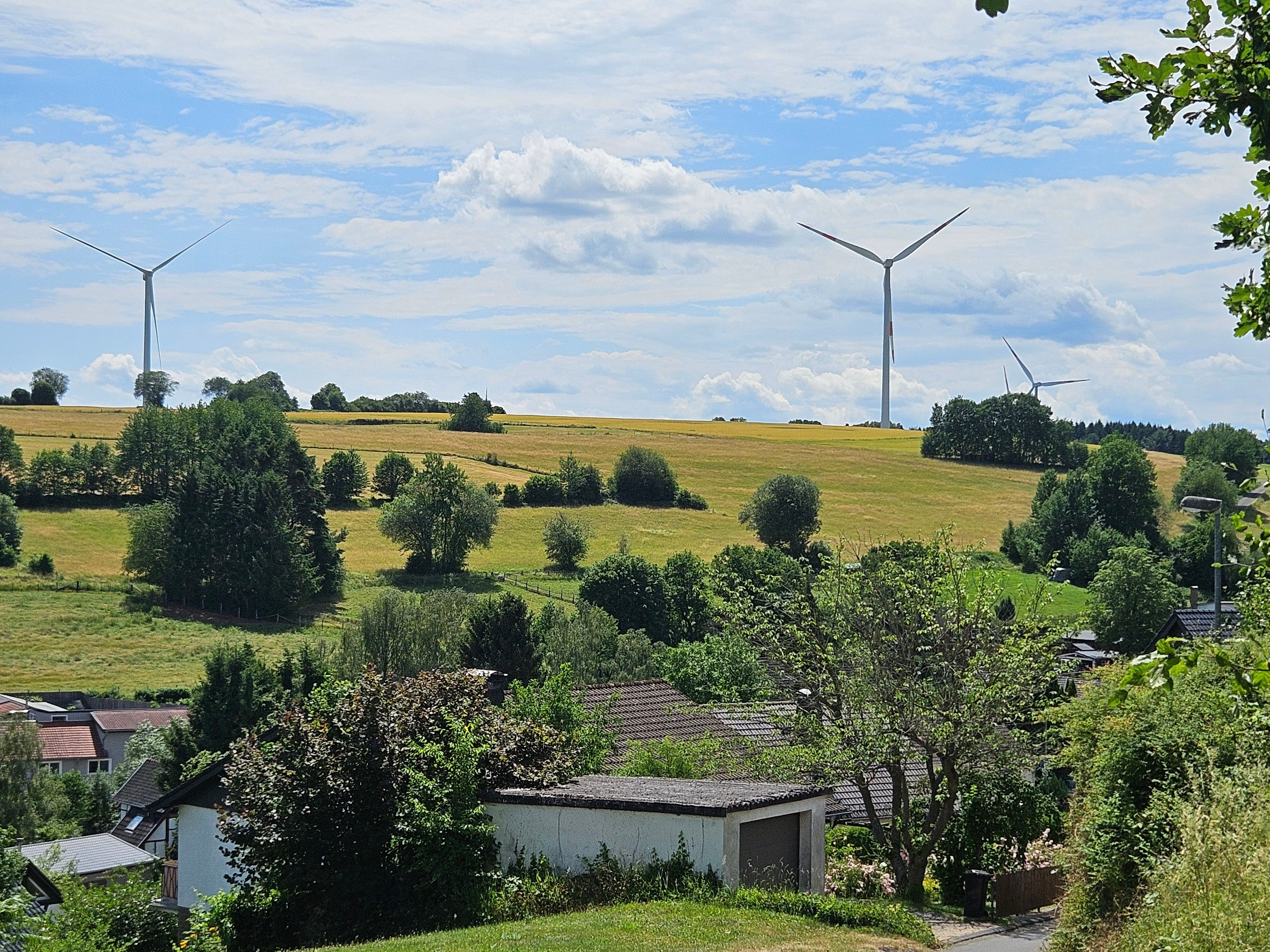 Das Foto zeigt die Windräder im Hintergrund und den Ort Golbach im Vordergrund.