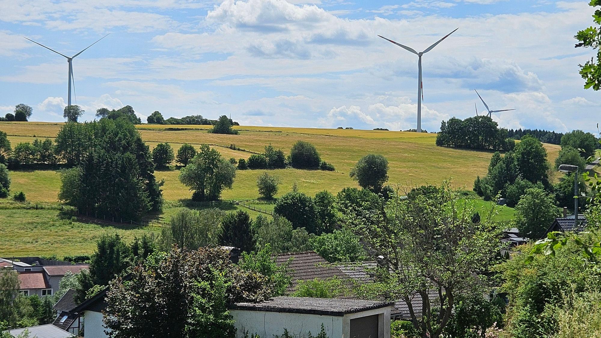Das Foto zeigt die Windräder im Hintergrund und den Ort Golbach im Vordergrund.