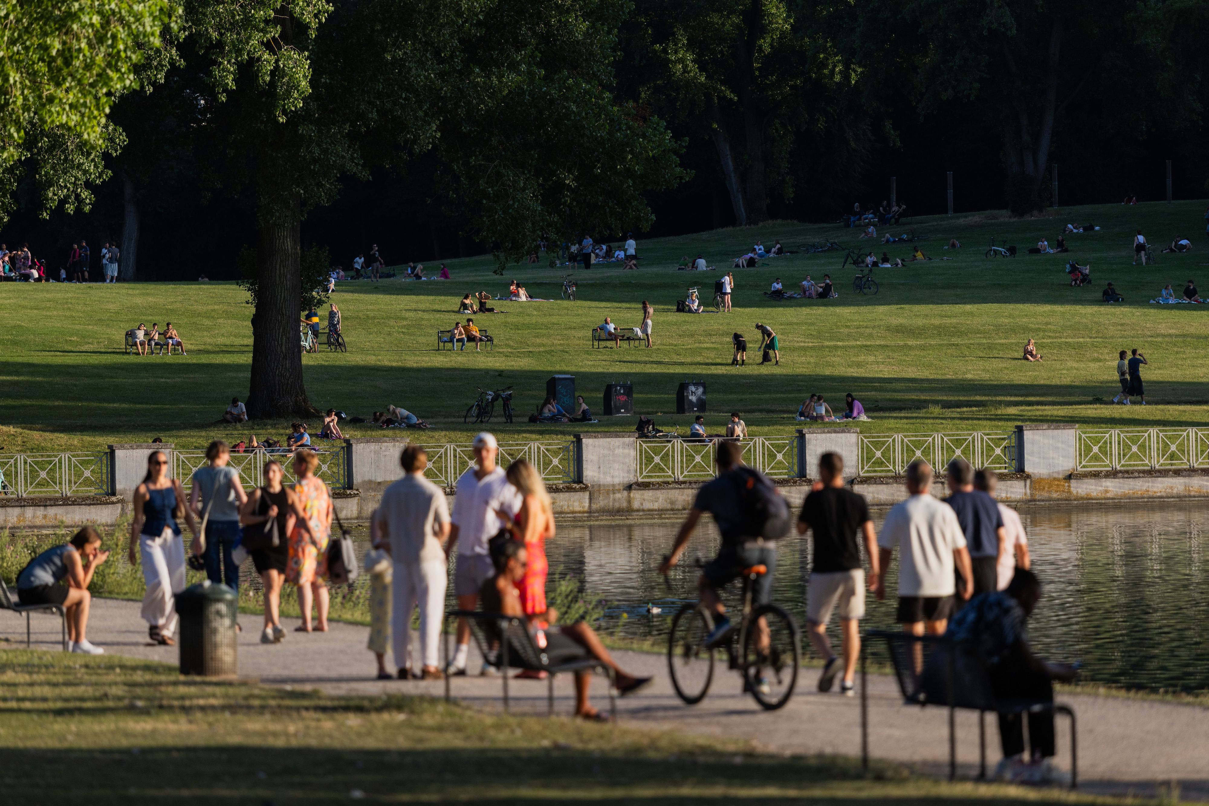 Menschen gehen in der Abendhitze am Aachener Weiher entlang.