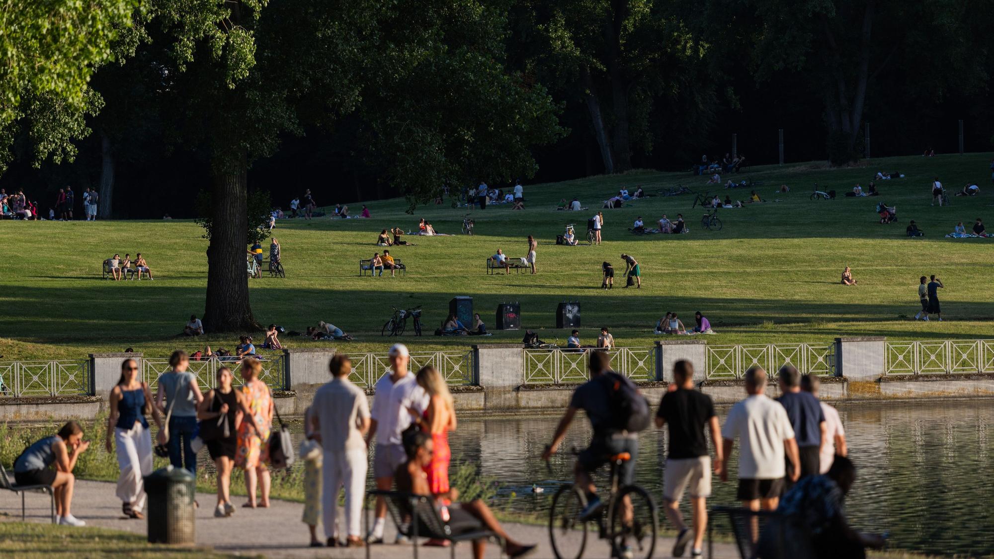 Menschen gehen in der Abendhitze am Aachener Weiher entlang.