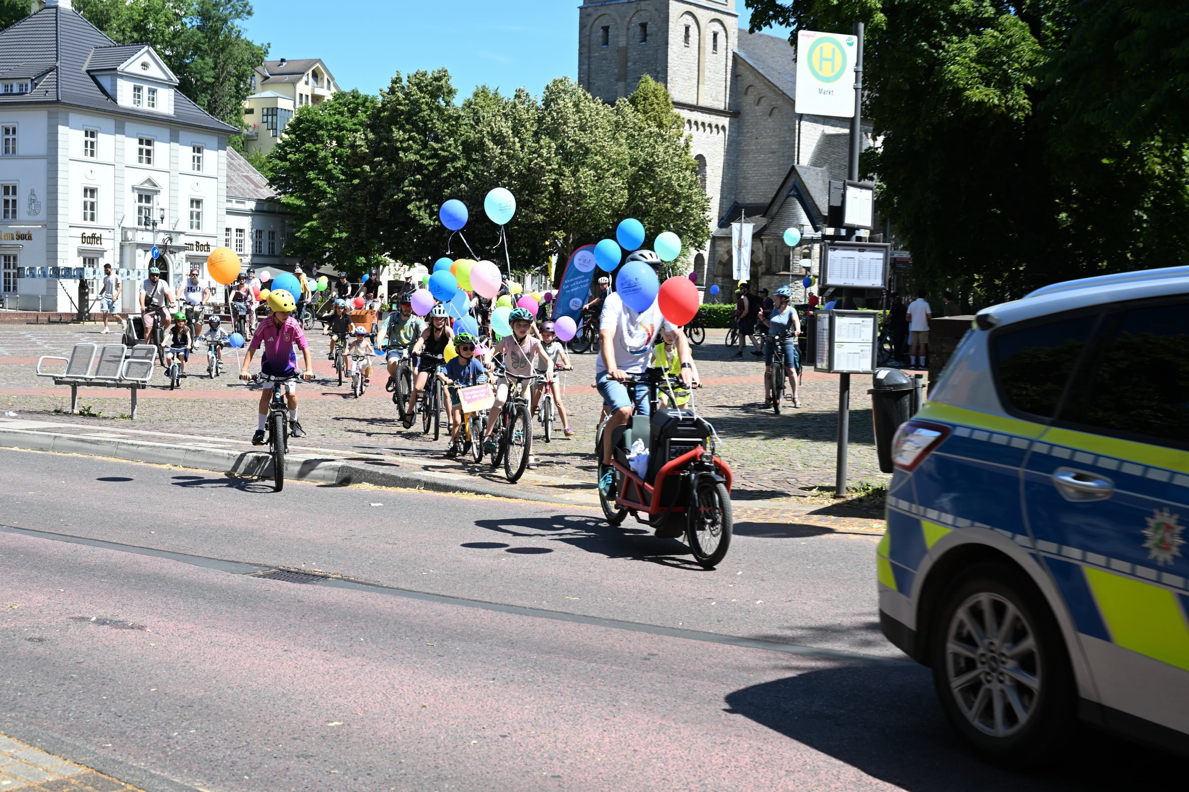 Fahrradfahrer mit bunten Luftballons hinter einem Polizeifahrzeug