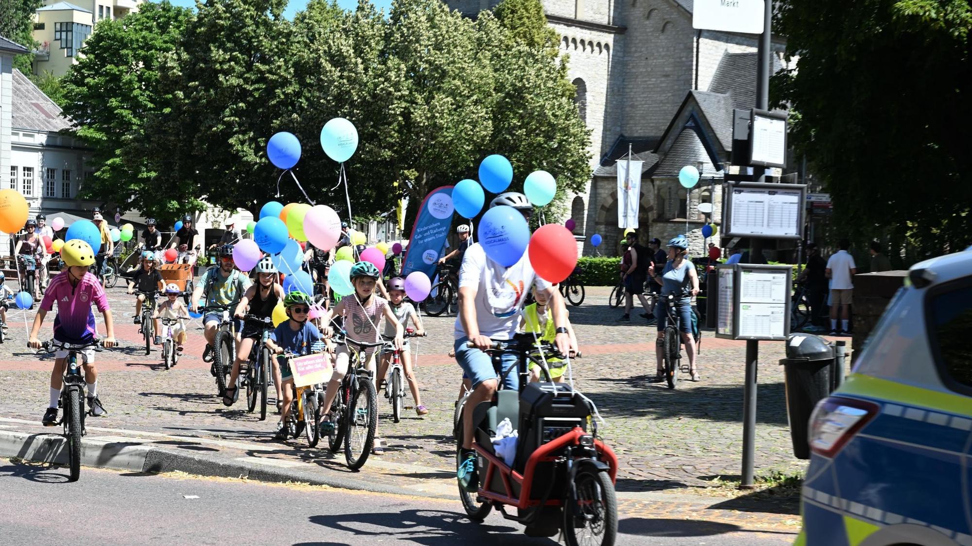 Fahrradfahrer mit bunten Luftballons hinter einem Polizeifahrzeug