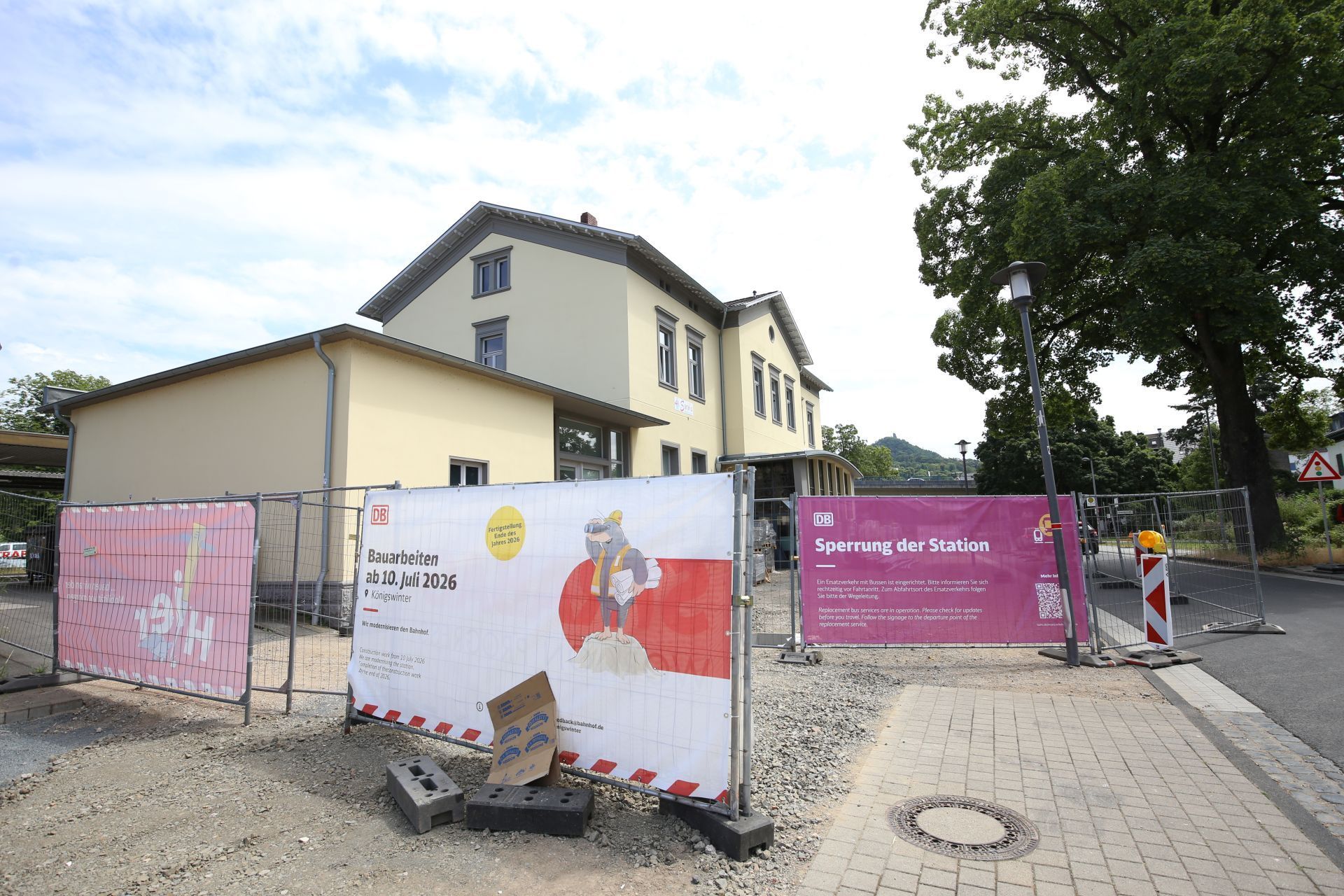 Ein kleiner Bahnhof; Bauzäune sperren das Gelände ab, Transparente weisen auf Bauarbeiten hin.