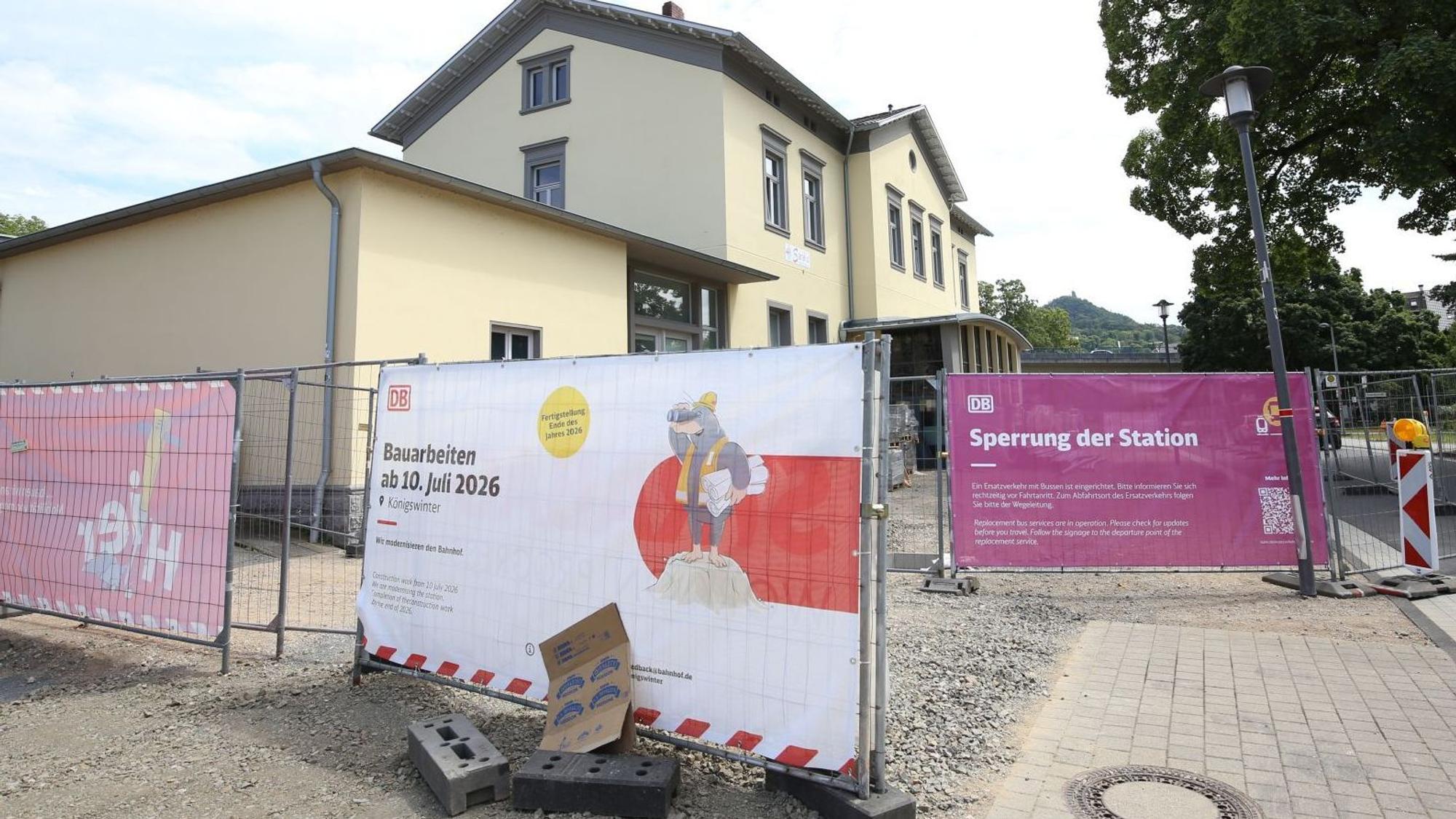 Ein kleiner Bahnhof; Bauzäune sperren das Gelände ab, Transparente weisen auf Bauarbeiten hin.