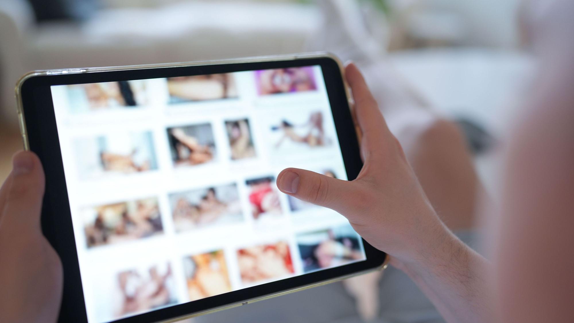 Das gestellte Foto zeigt einen Mann, der auf einen Smartphone eine Porno-Internetseite anschaut.