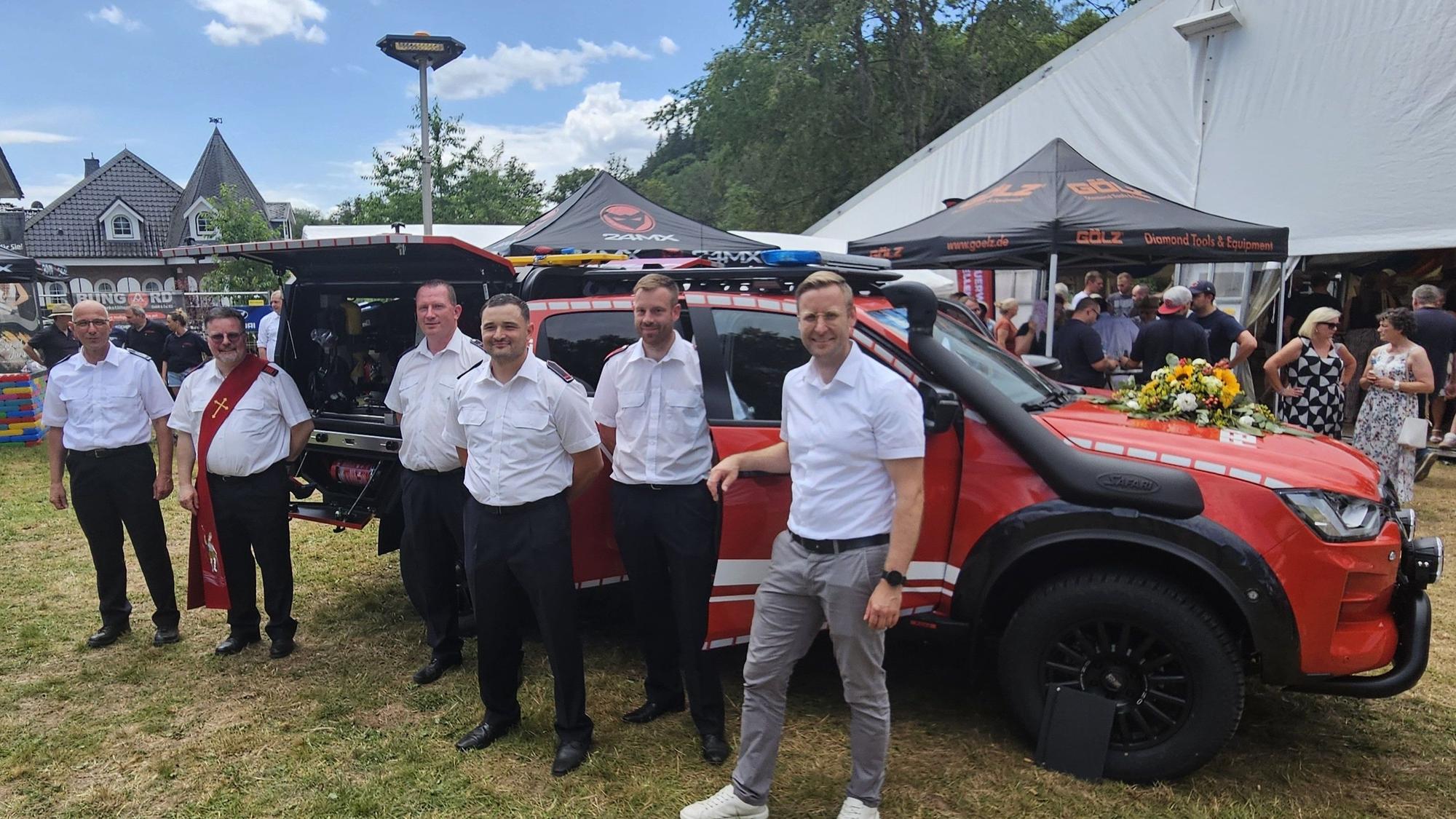 Sechs Männer, zum Teil in Feuerwehruniform, stehen vor dem neuen Fahrzeug.