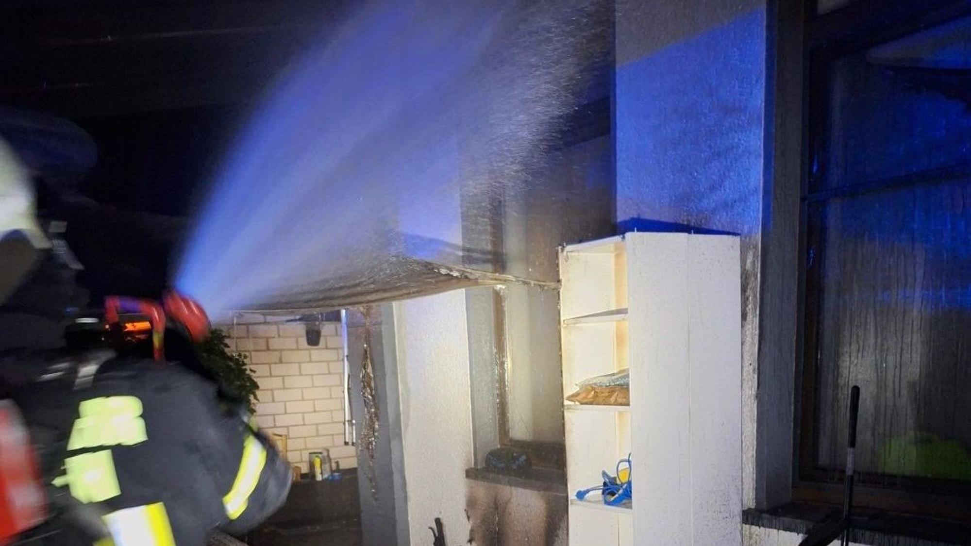 Ein Feuerwehrmann löscht einen Brand an einer Hauswand.