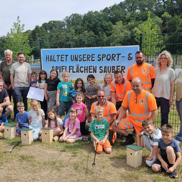 Die Helfer und die Kinder stehen und knien vor einem Banner mit der Aufschrift „Haltet unsere Sport- und Spielflächen sauber“.