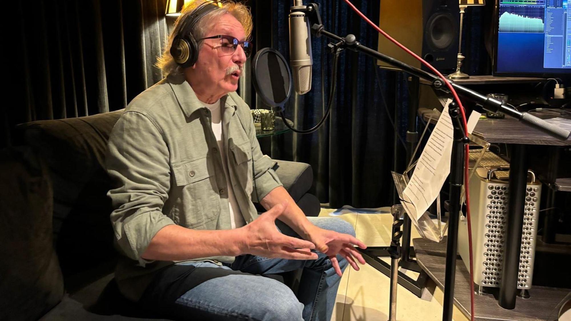 Ein Mann sitzt in einem Aufnahmestudio und singt ins Mikro.
