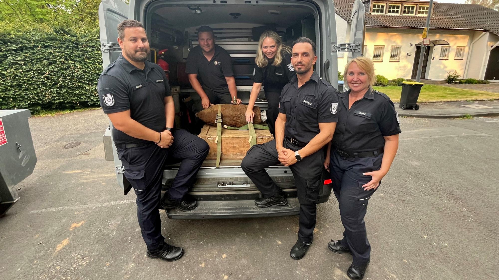 Karsten Olbrich, Silvana Hoffmann, Caner Boztepe und Petra Rothe (Leitungsteam Ordnungsamt) und hinten Philipp Blens (KBD Rheinland der Bezirksregierung Düsseldorf) zeigen den entschärften Blindgänger, der in einem Kleintransporter liegt.