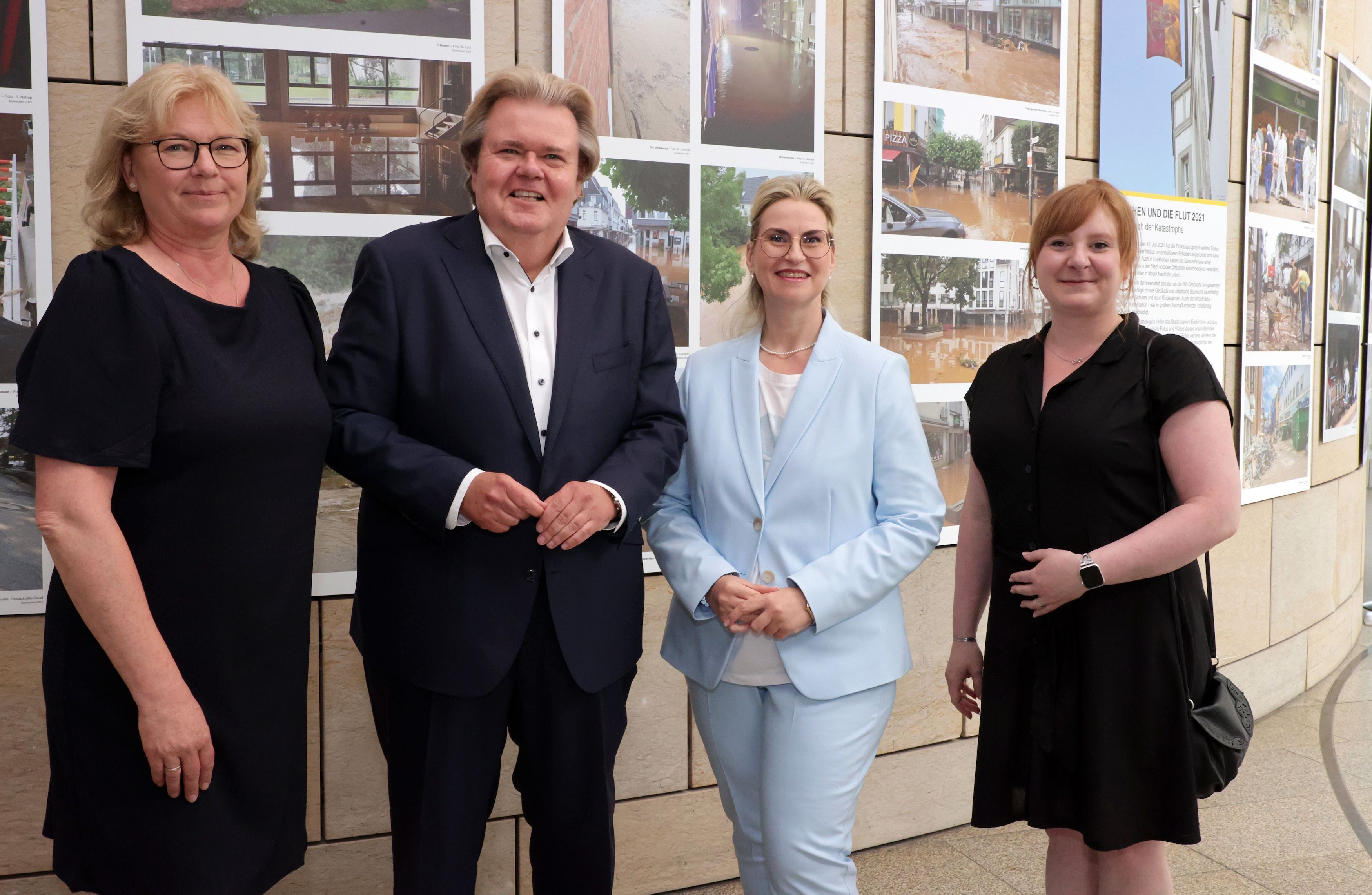 Klaus Voussem steht mit drei Damen vor Bildern einer Ausstellung.