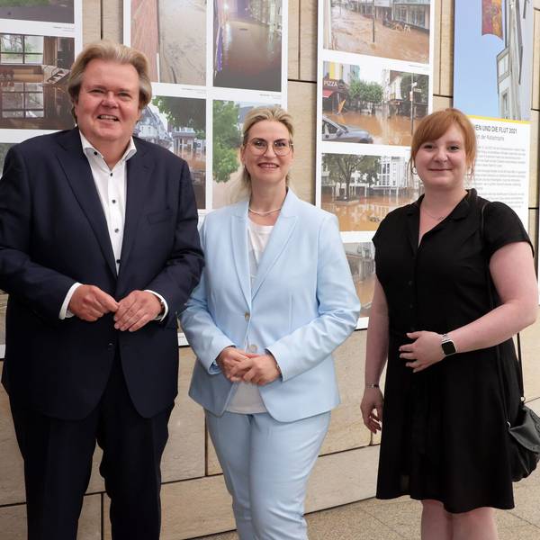 Klaus Voussem steht mit drei Damen vor Bildern einer Ausstellung.