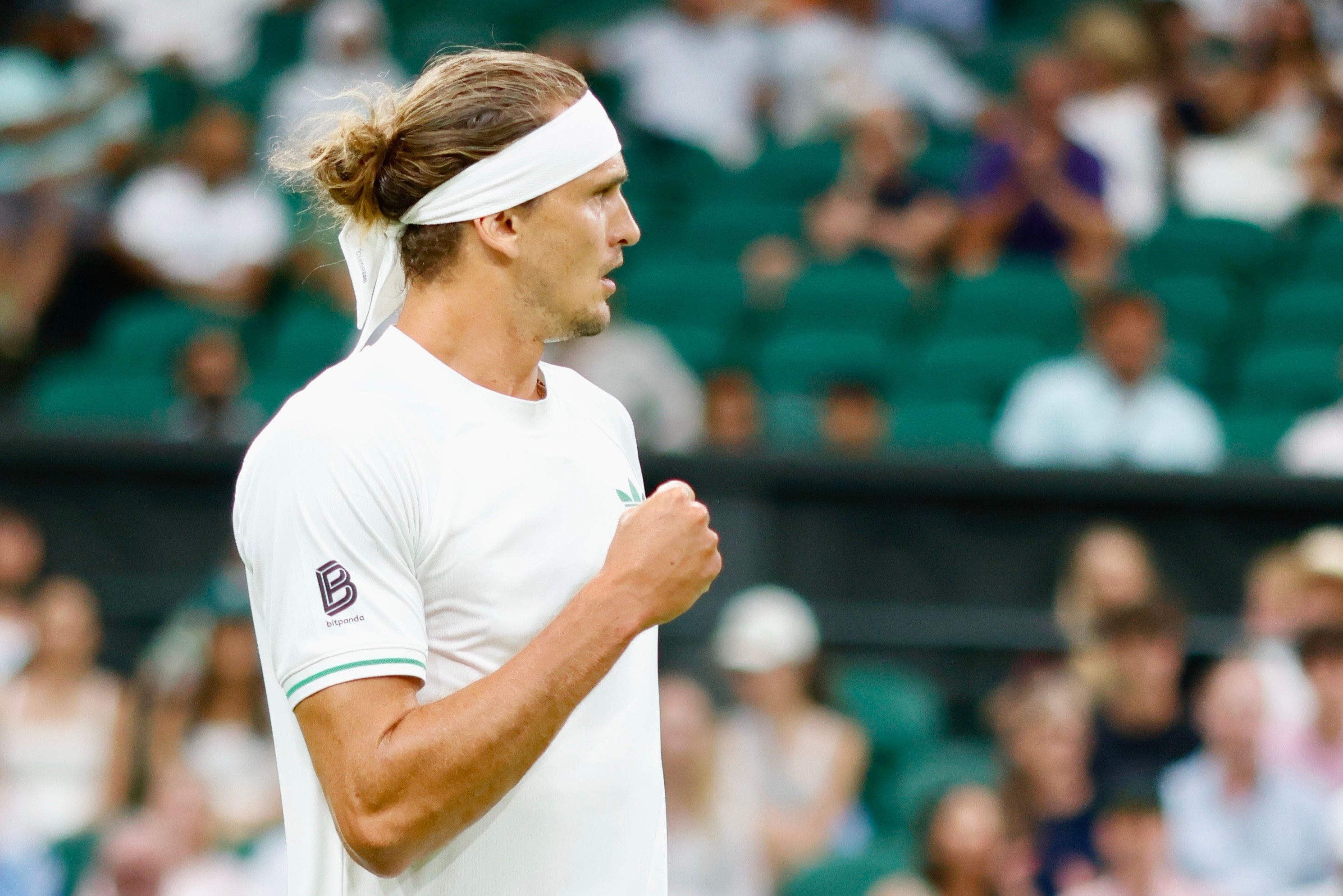 Alexander Zverev steht auf dem Tennisplatz und zeigt die Faust. Er hat ein weißes Shirt und ein weißes Stirnband an.