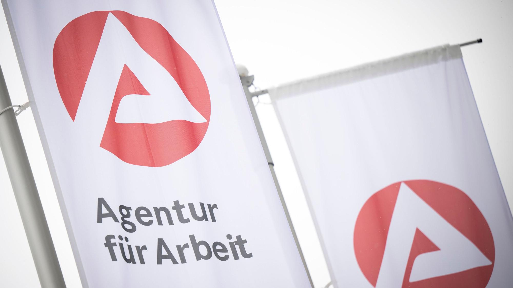 Fahnen mit dem Logo der Agentur für Arbeit wehen im Wind.