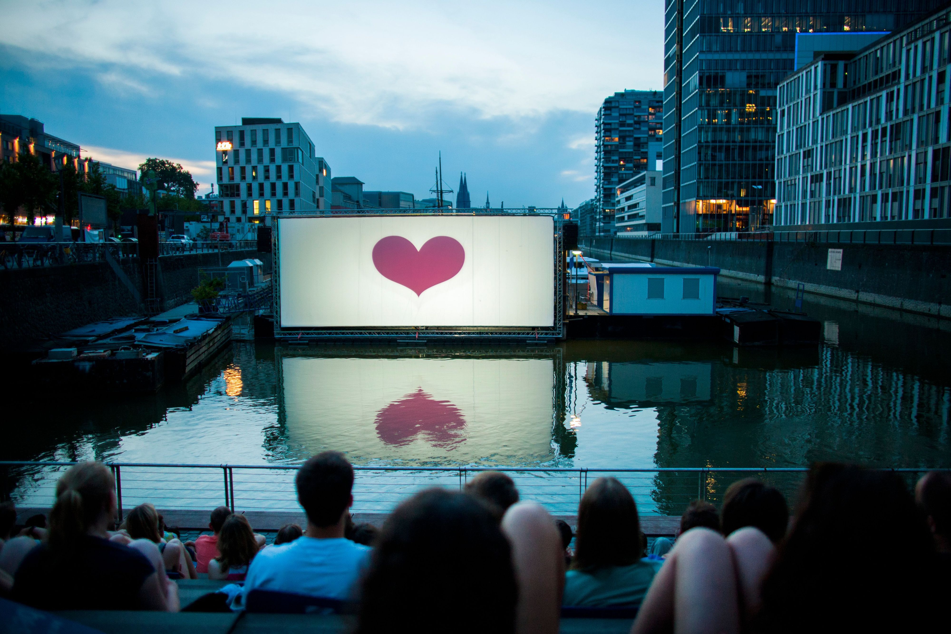 Im Open-Air-Kino am Rheinauhafen vor der Domkulisse warten Besucher auf die Filmvorführung. (Archivbild)