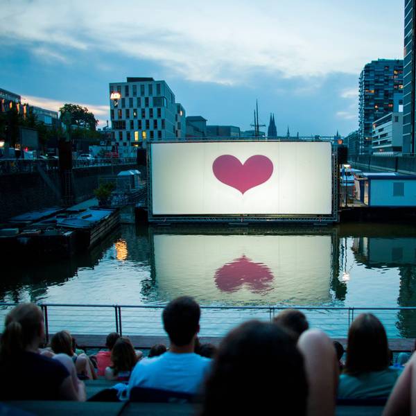 Im Open-Air-Kino am Rheinauhafen vor der Domkulisse warten Besucher auf die Filmvorführung. (Archivbild)