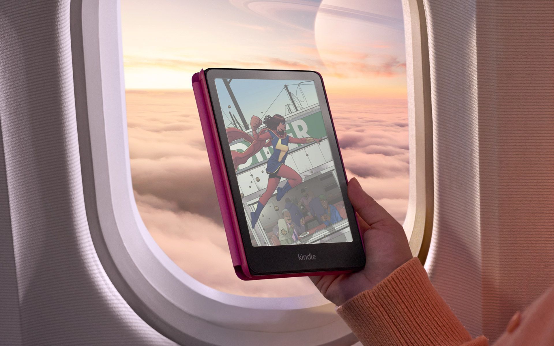 Amazon Kindle Colorsoft Signature Edition in einer Hand vor einem Flugzeugfenster, auf dem Display eine farbige Comic-Szene mit einer Superheldin.