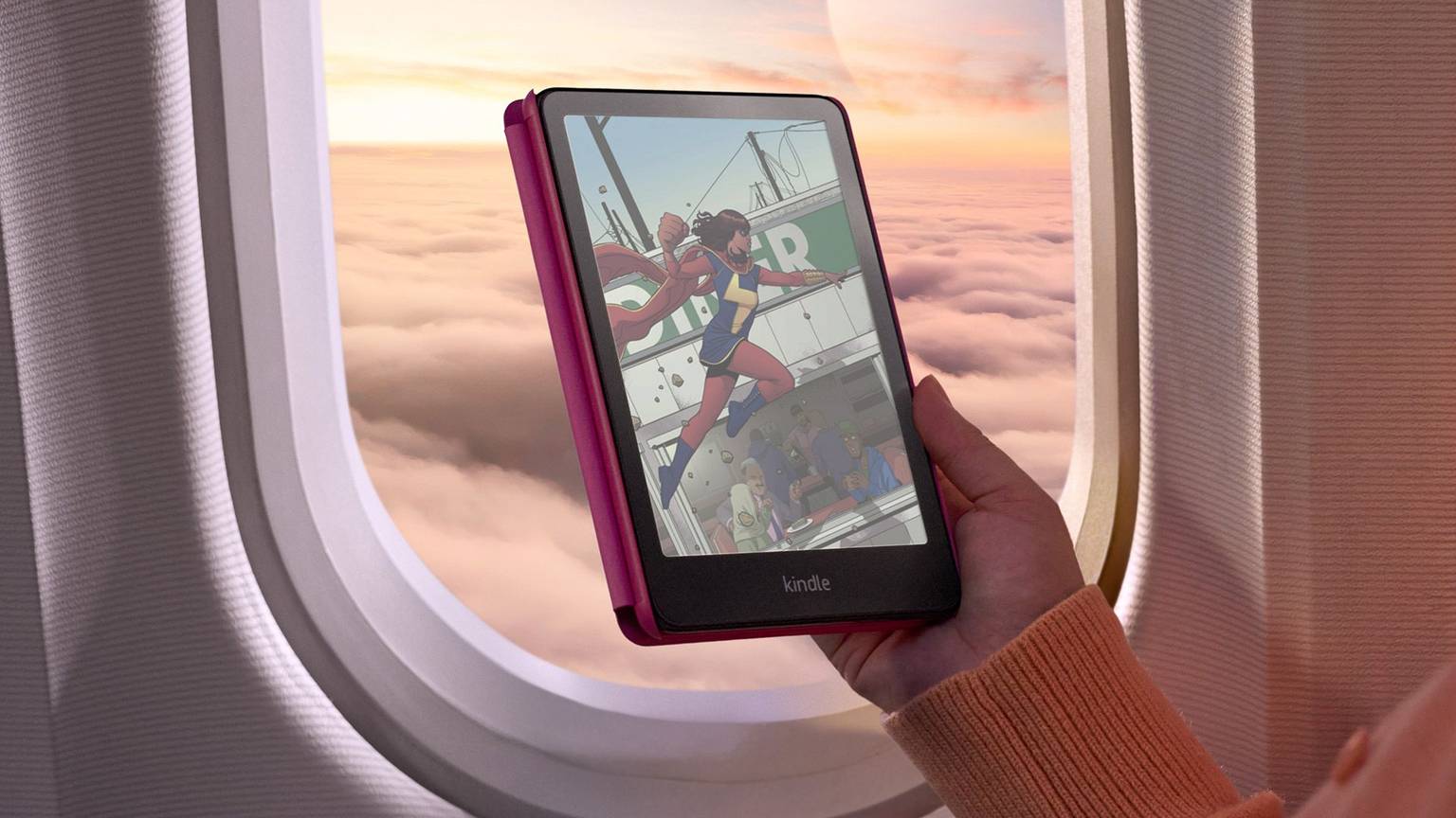 Amazon Kindle Colorsoft Signature Edition in einer Hand vor einem Flugzeugfenster, auf dem Display eine farbige Comic-Szene mit einer Superheldin.