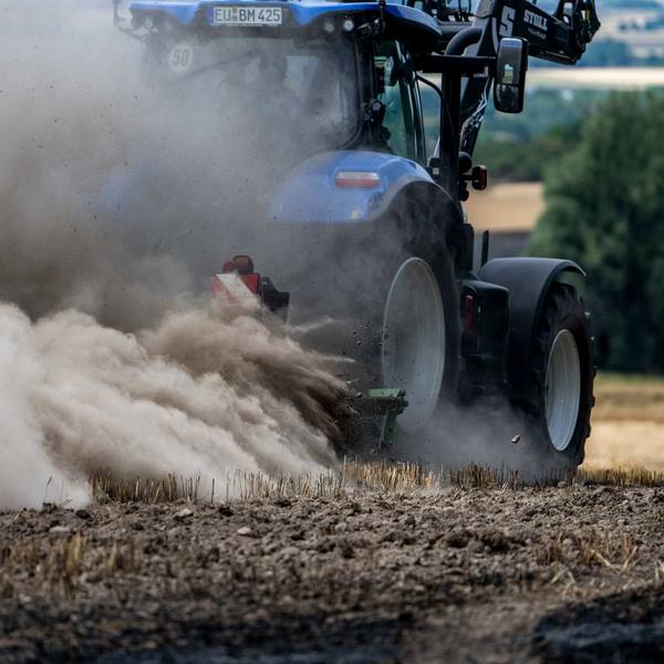 Ein blauer Traktor fährt über ein Stoppelfeld, von dem Rauch aufsteigt.