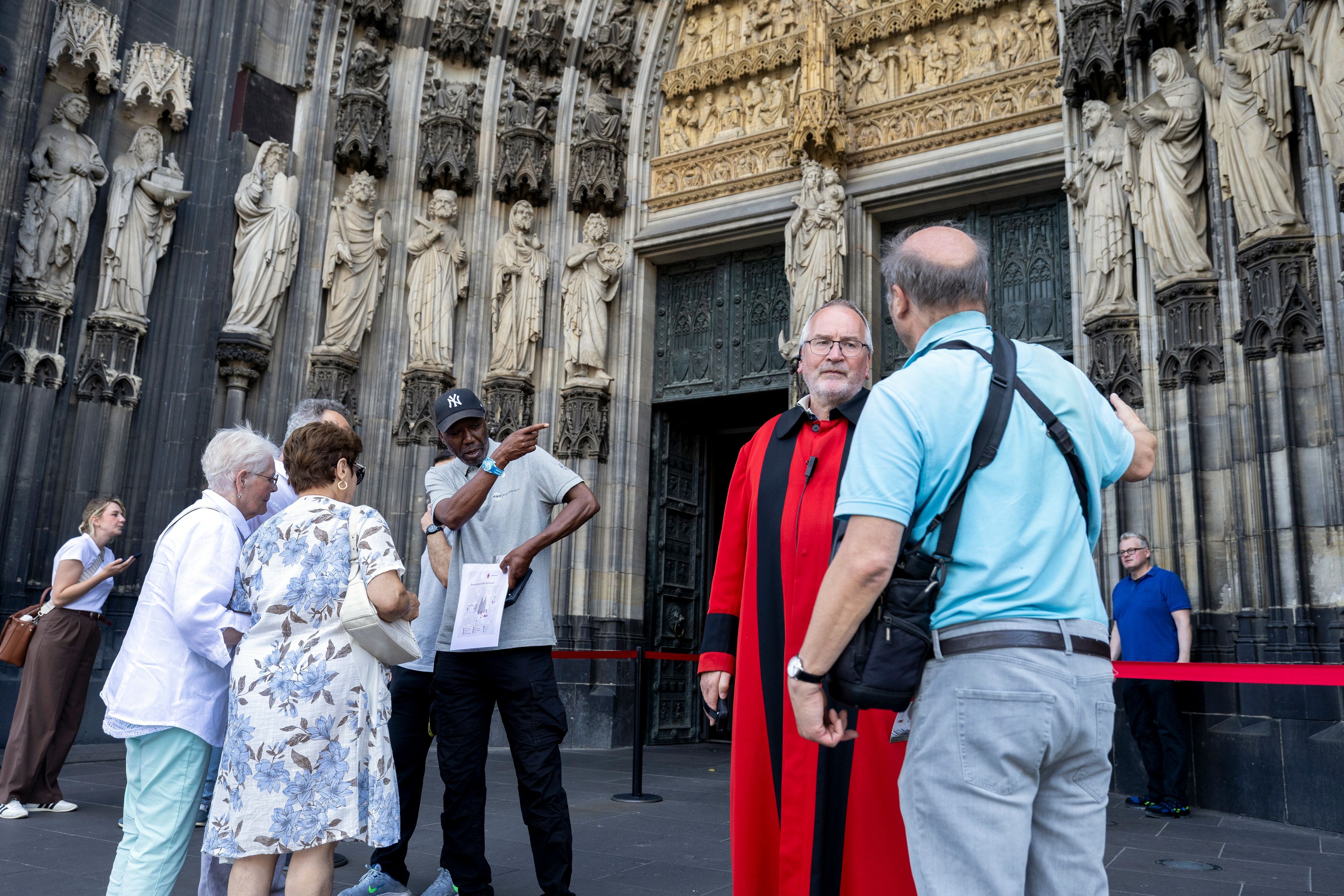 Domschweizer und Servicekräfte informieren Menschen vor dem Kölner Dom über die neuen Besuchsregeln.