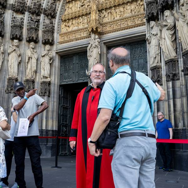 Domschweizer und Servicekräfte informieren Menschen vor dem Kölner Dom über die neuen Besuchsregeln.