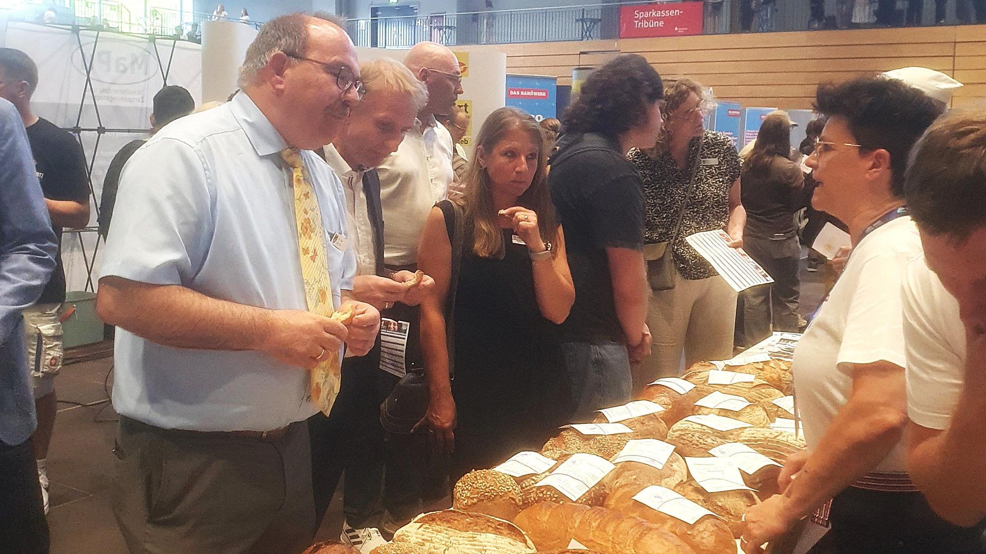 Zwei Männer und einige Frauen stehen an einem Stand mit Broten.
