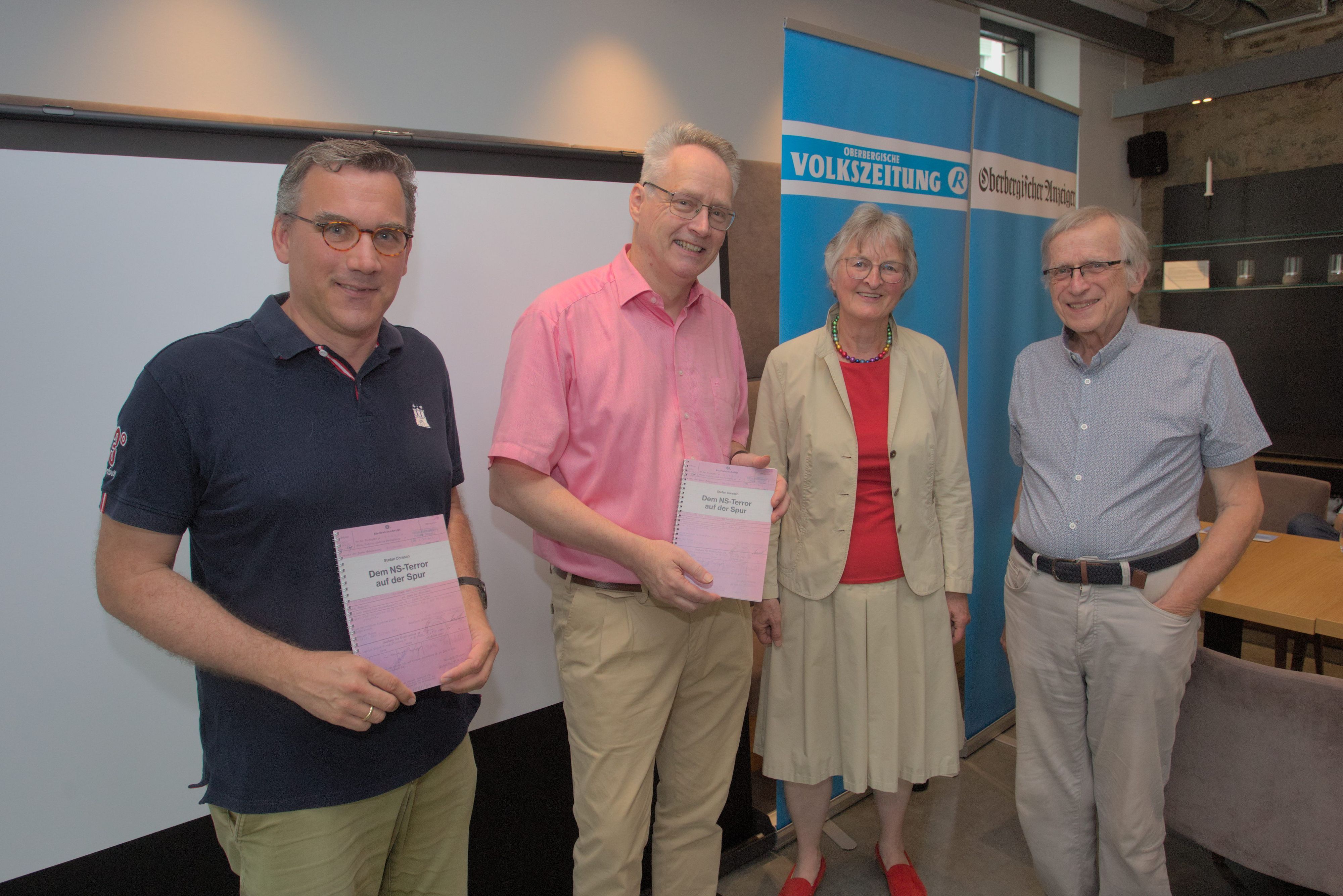 Drei Männer und eine Frau zeigen ein Buch.