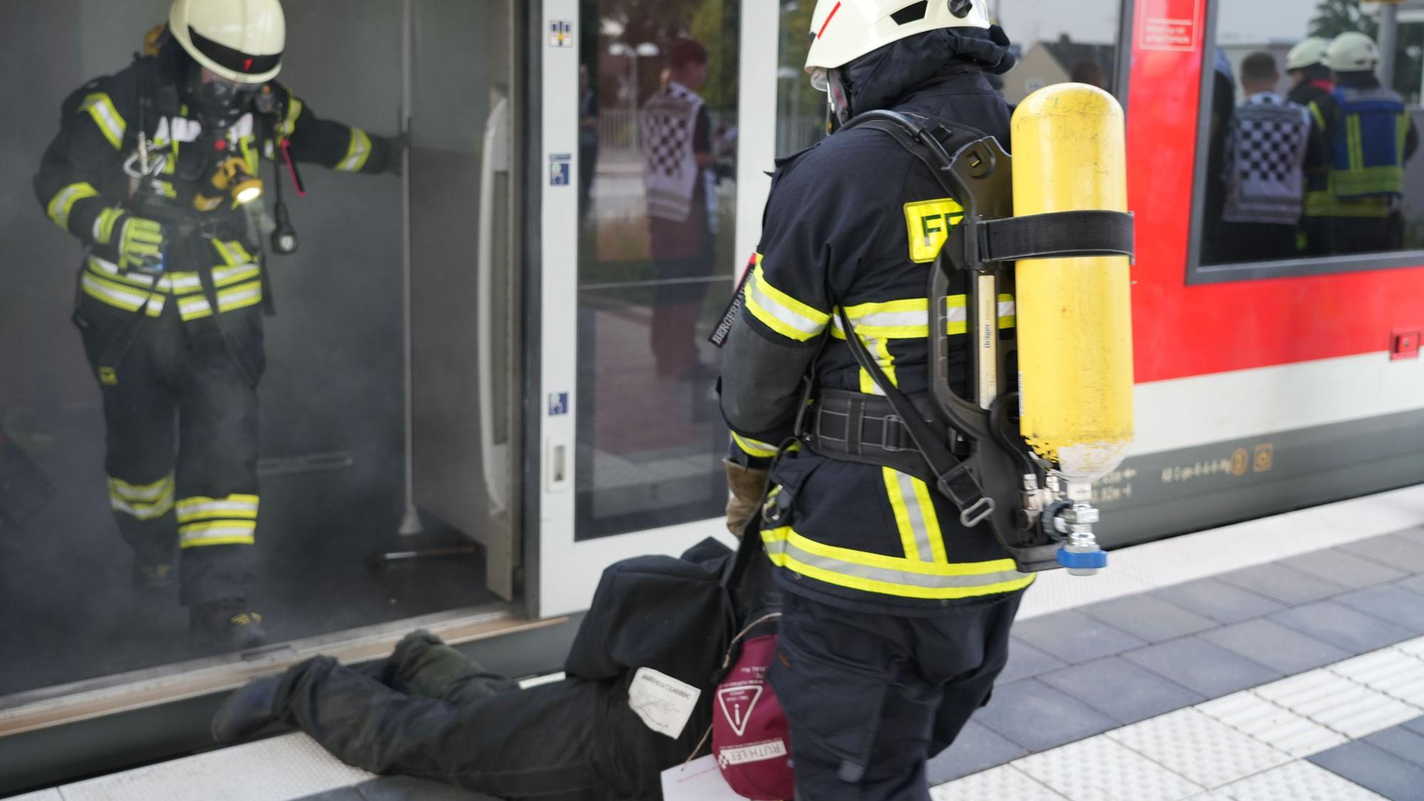 Eine Feuerwehrkraft zieht einen Mann aus einem qualmenden Zugabteil.