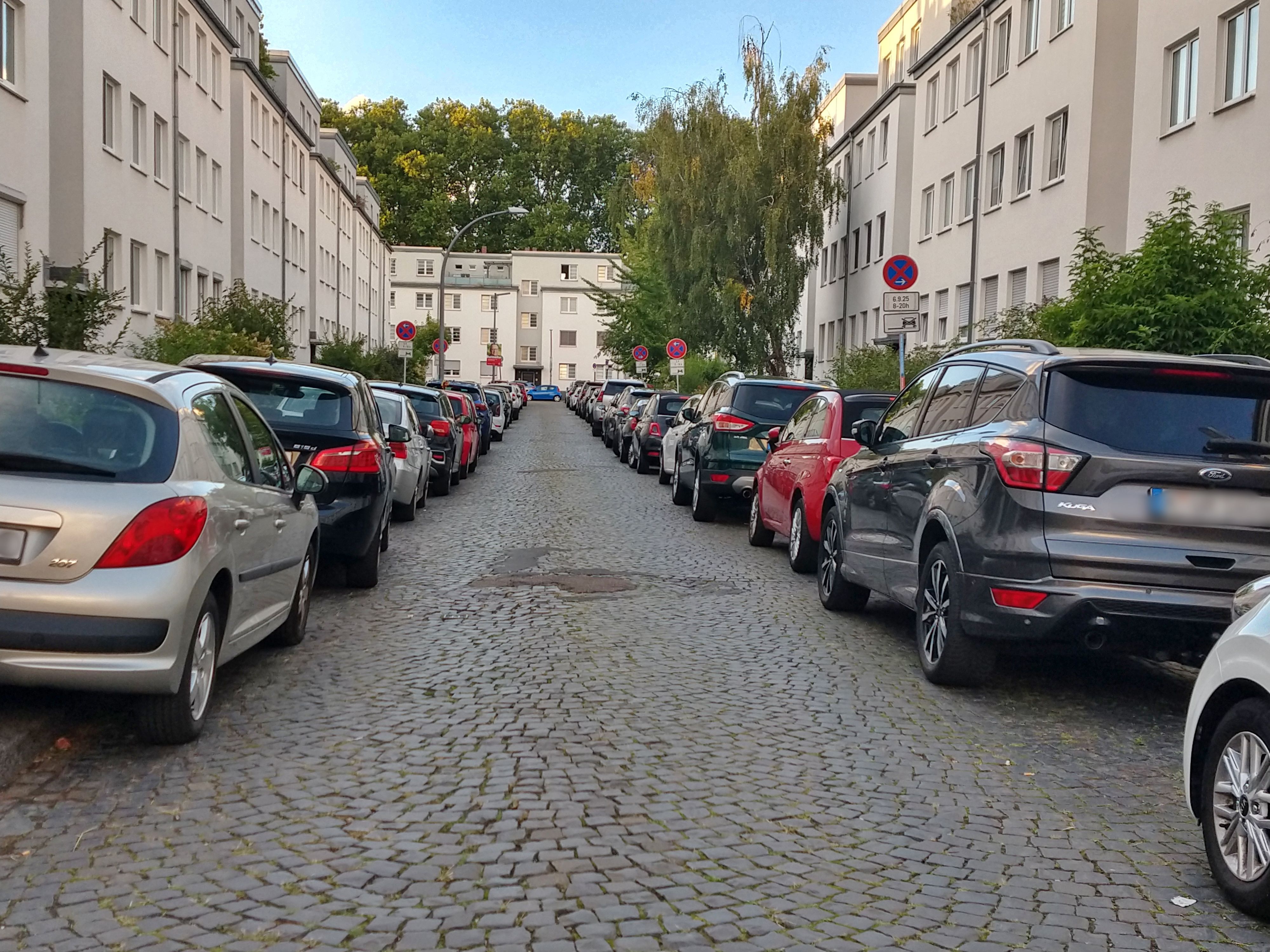 Links und rechts einer schmalen Straße mit Kopfsteinpflaster parken Autos.