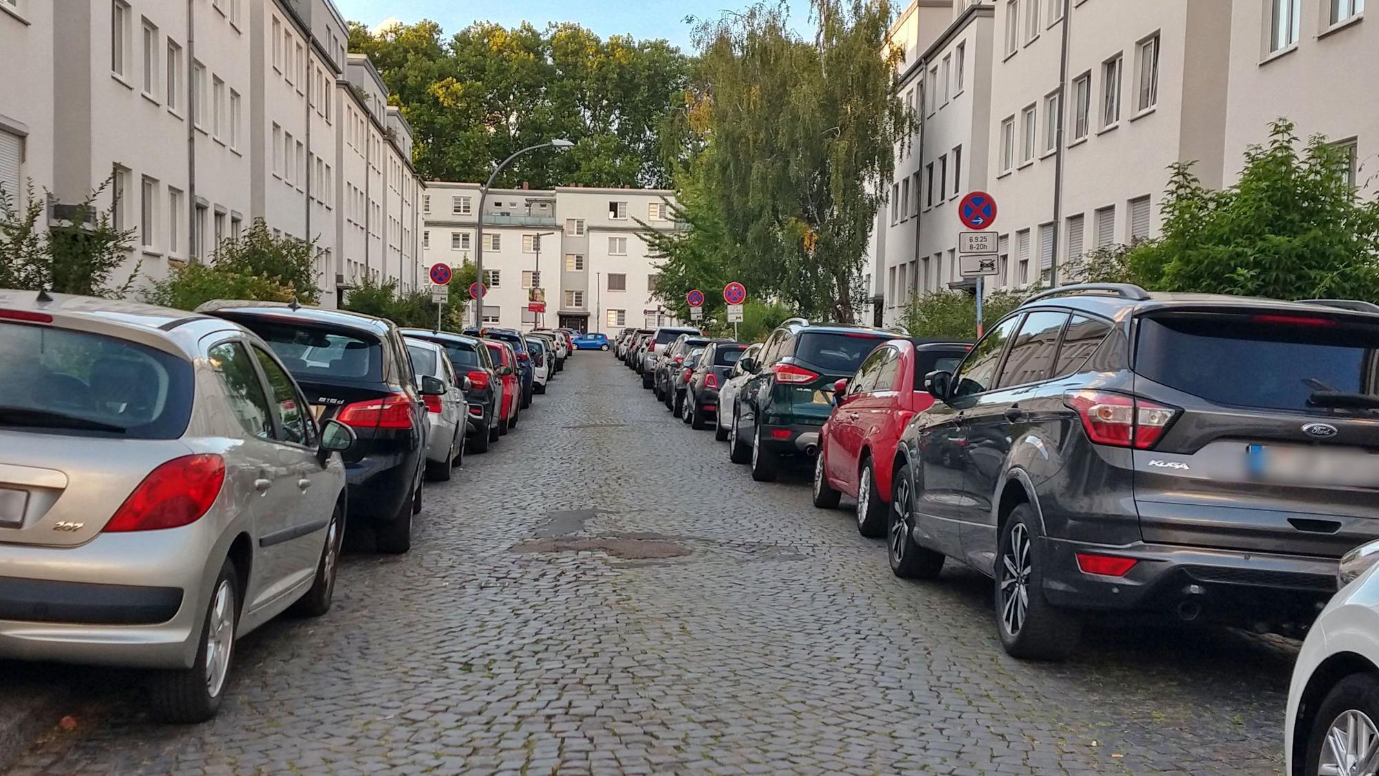 Links und rechts einer schmalen Straße mit Kopfsteinpflaster parken Autos.