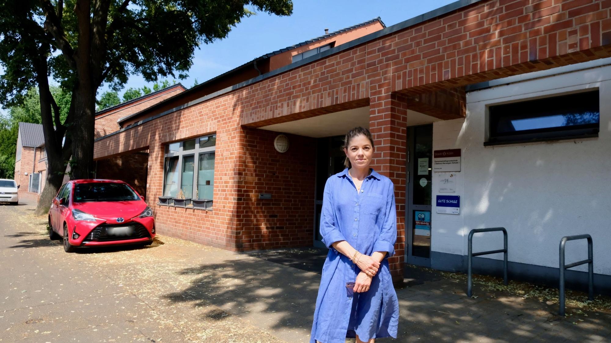 Eine junge Frau im blauen Kleid steht vor dem Eingang einer Schule.