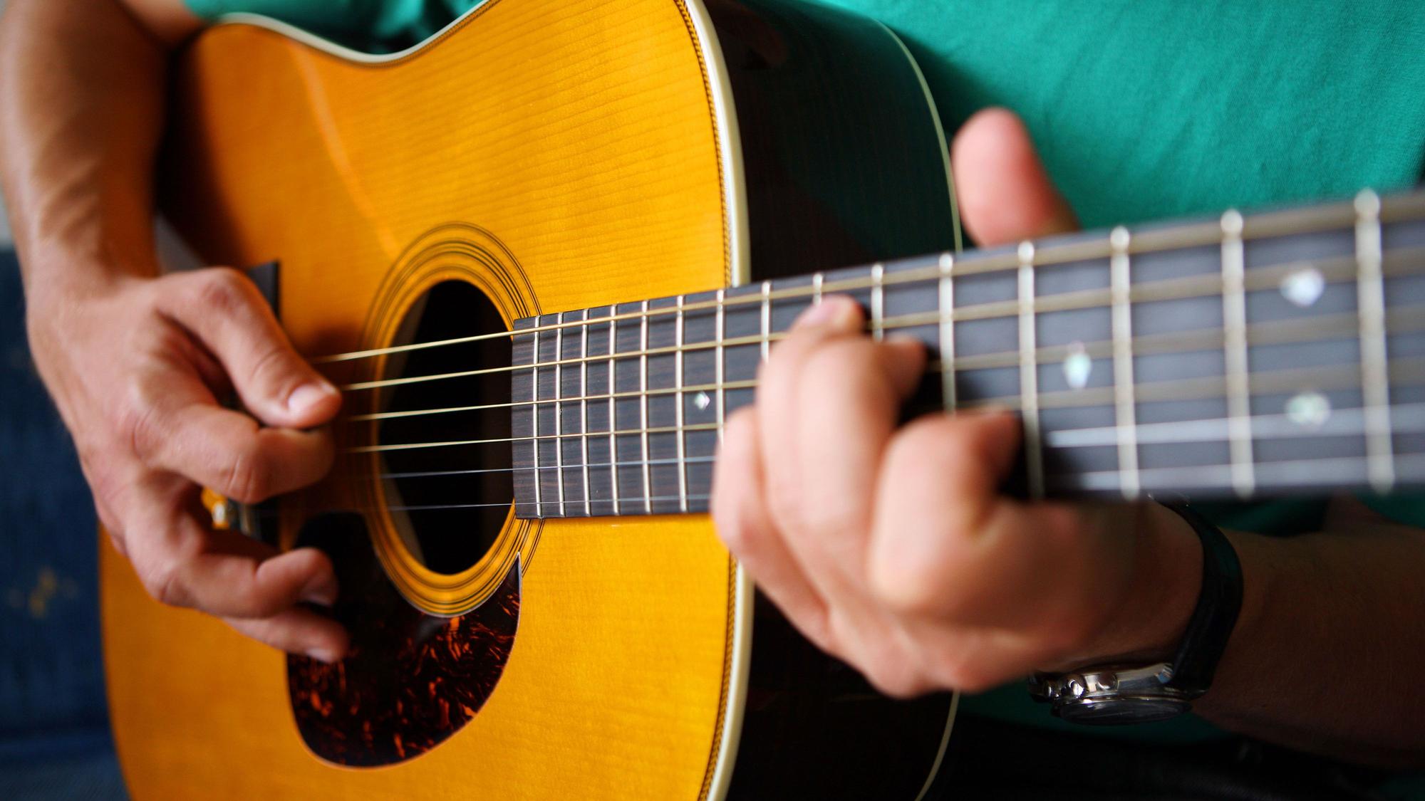 Ein Gitarrist spielt auf einer Stahlsaiten Dreadnought Akustikgitarre.