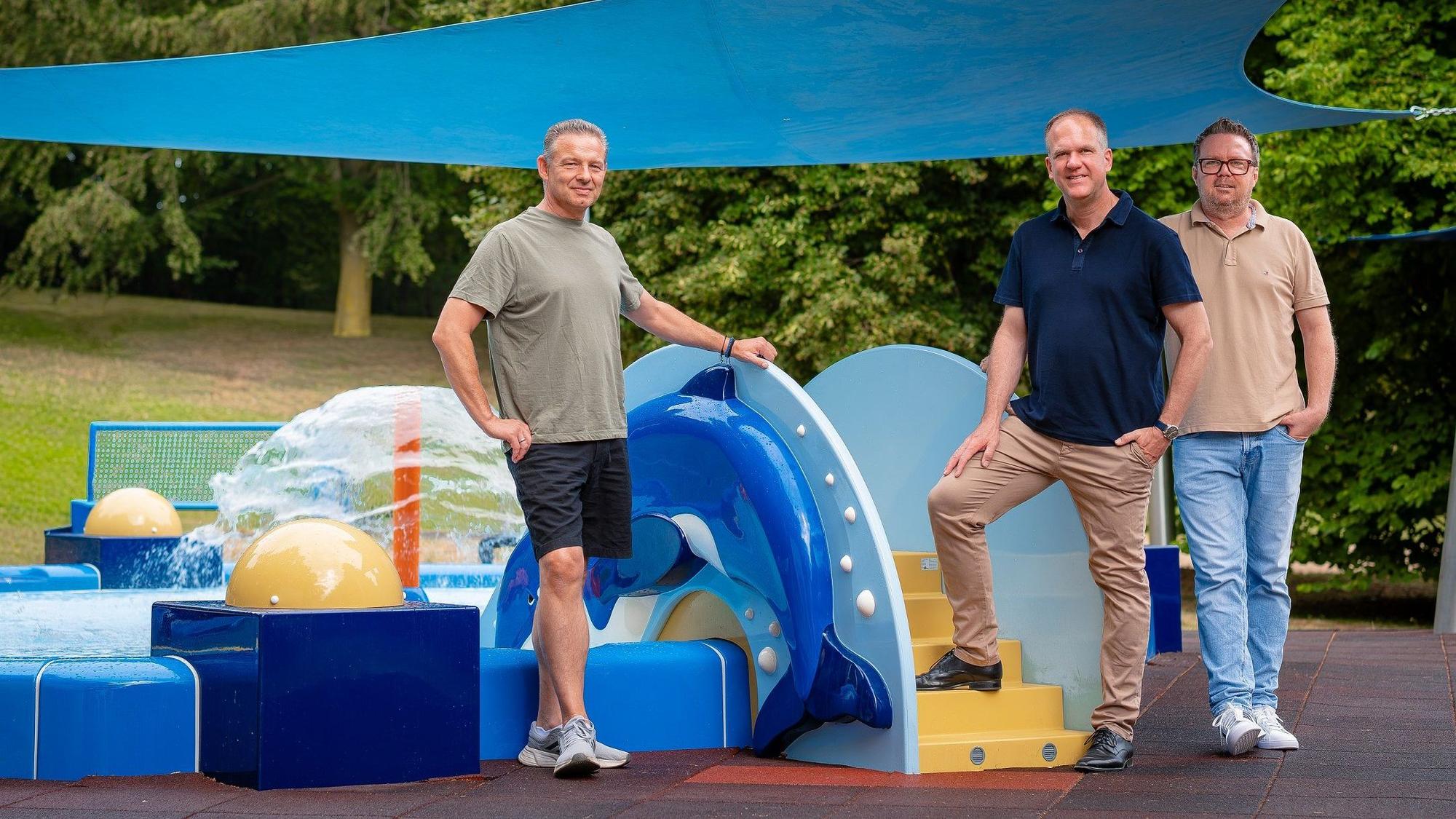 Das Foto zeigt die Vertreter der Stadt vor den farbenfrohen Spielgeräten auf dem neuen Wasserspielplatz.