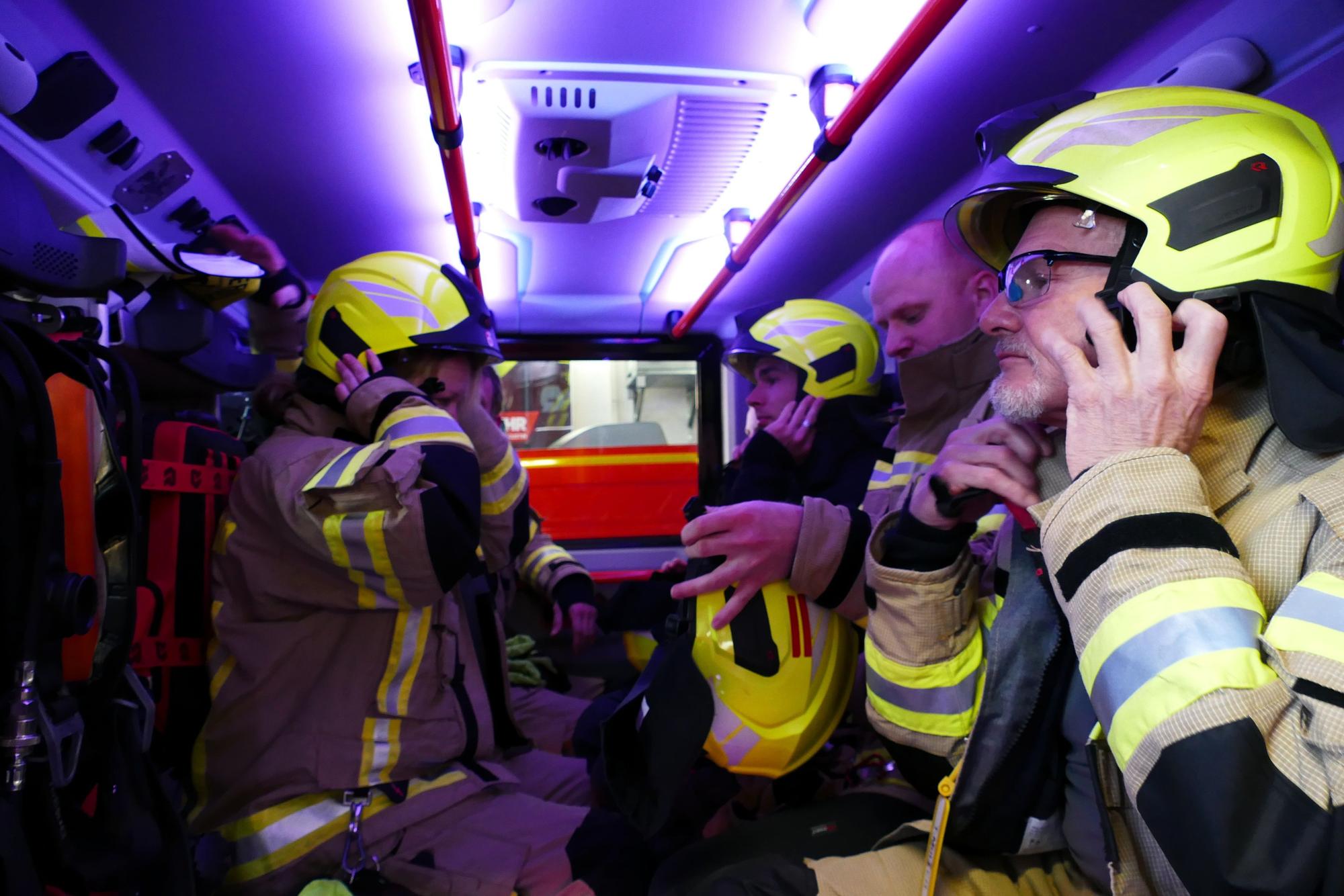Auf der Fahrt zum Einsatzort setzen die Feuerwehrleute ihre Helme auf und streifen sich die Atemschutzgeräte über.