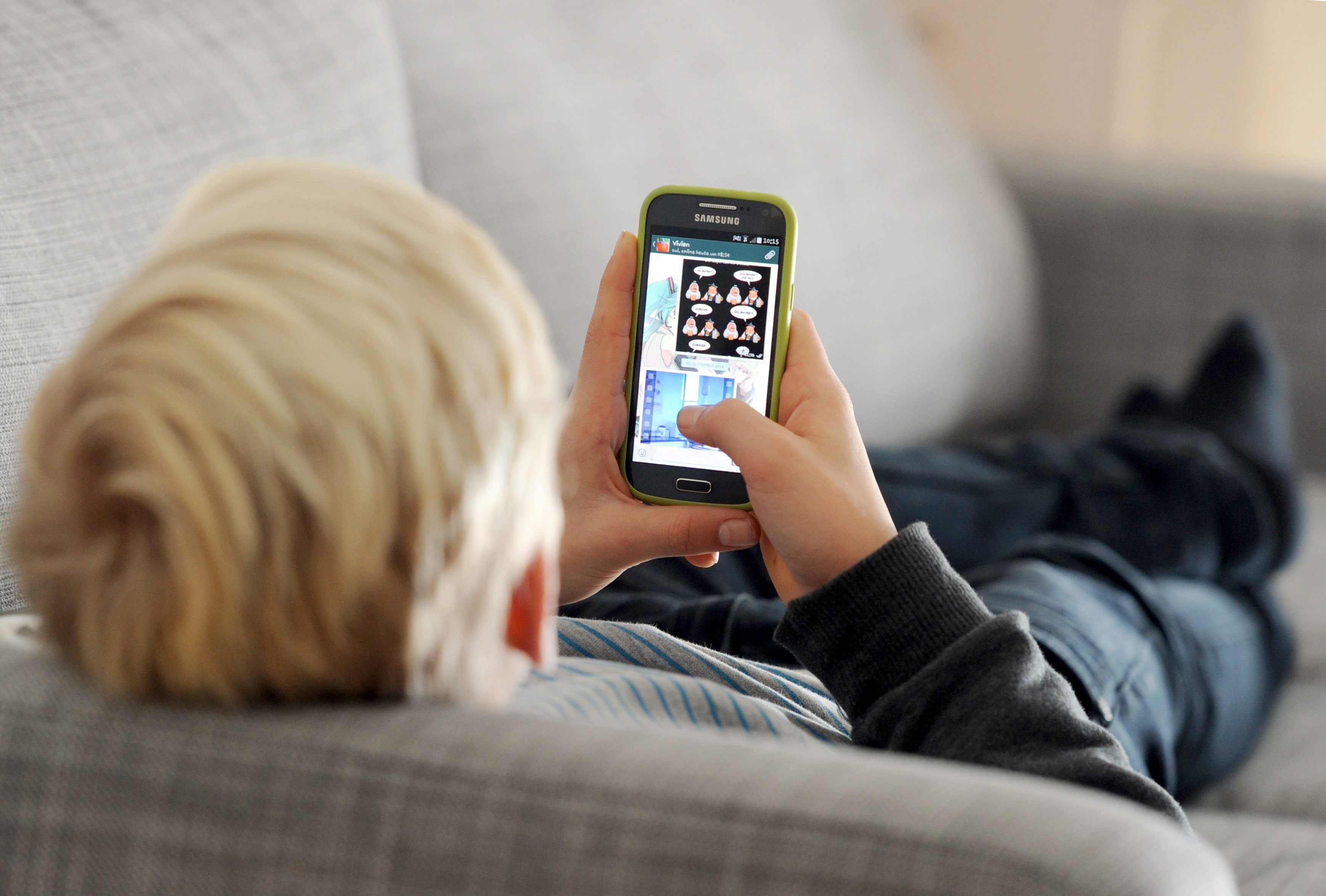 Ein Kind liegt auf einem Sofa und blickt auf sein Smartphone.