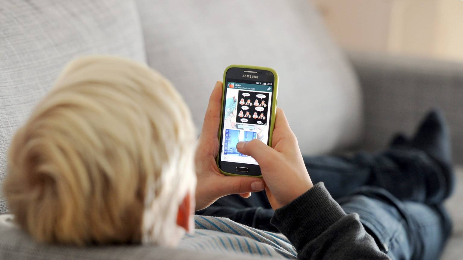 Ein Kind liegt auf einem Sofa und blickt auf sein Smartphone.