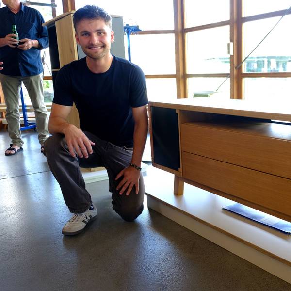 Jan Beyers kniet neben einem Sideboard mit Massivholzdetails, das vor einer Fensterfront steht.