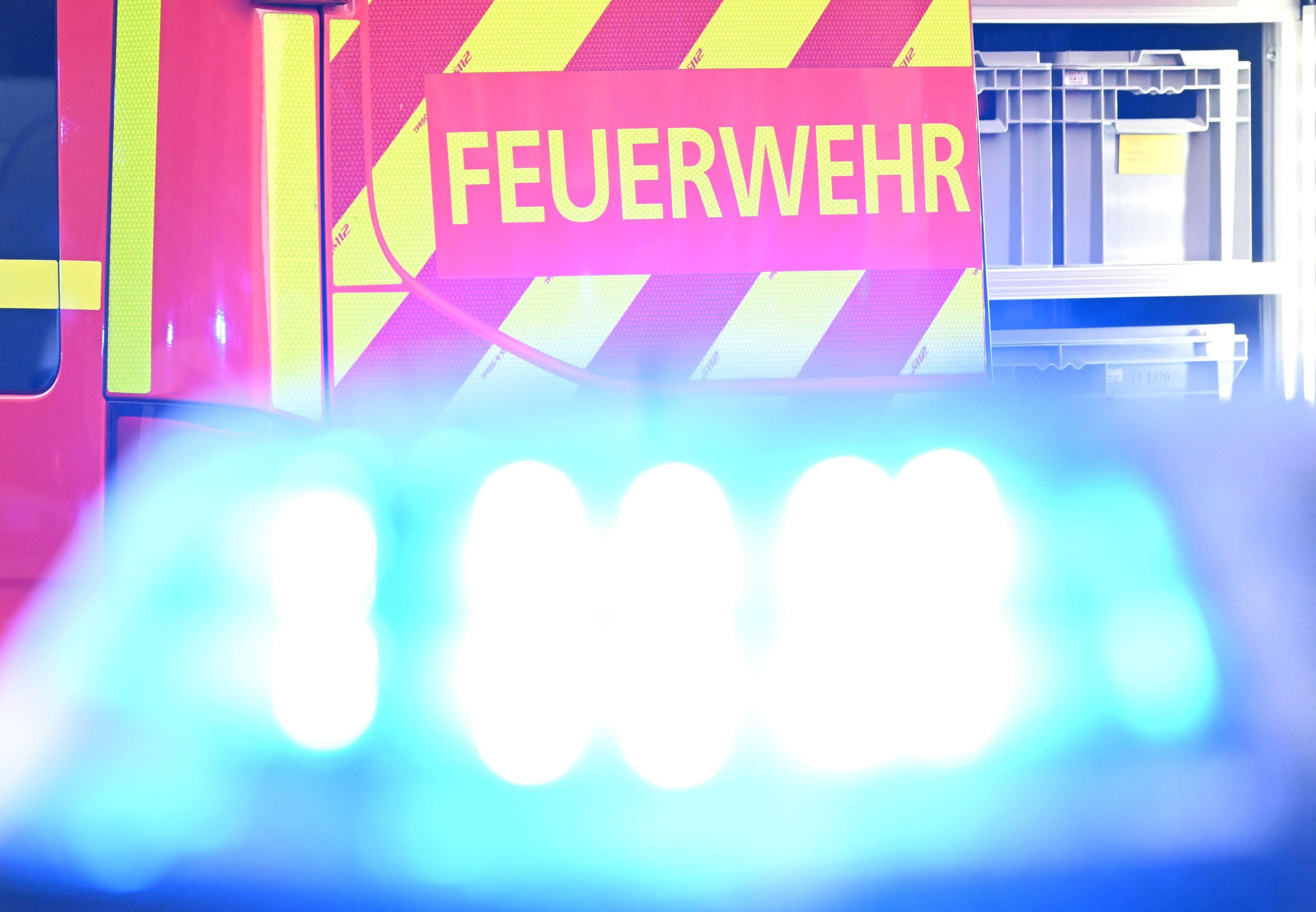 Ein Fahrzeug der Feuerwehr steht bei einem Einsatz auf einer Straße, während im Vordergrund das Blaulicht eines Polizeifahrzeugs zu sehen ist.