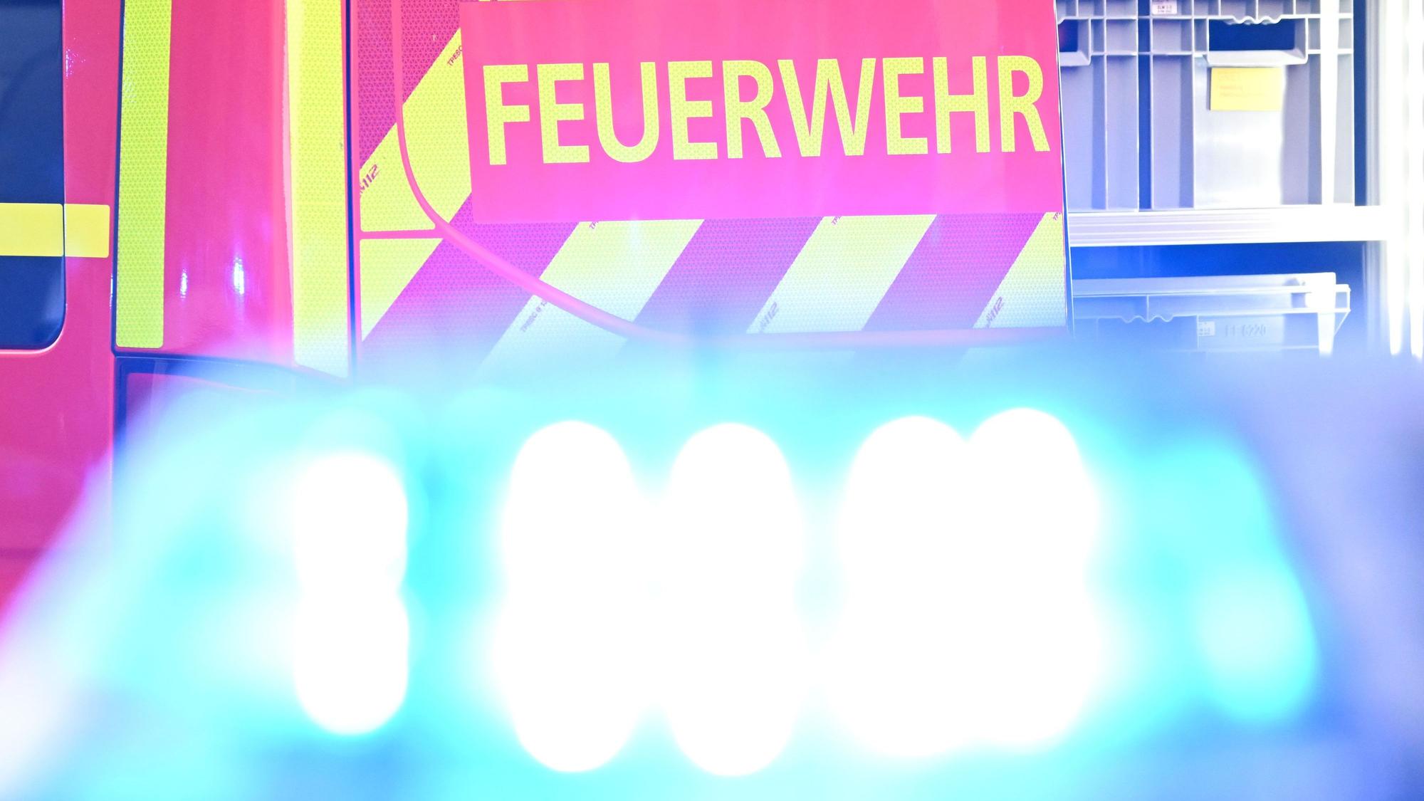 Ein Fahrzeug der Feuerwehr steht bei einem Einsatz auf einer Straße, während im Vordergrund das Blaulicht eines Polizeifahrzeugs zu sehen ist.
