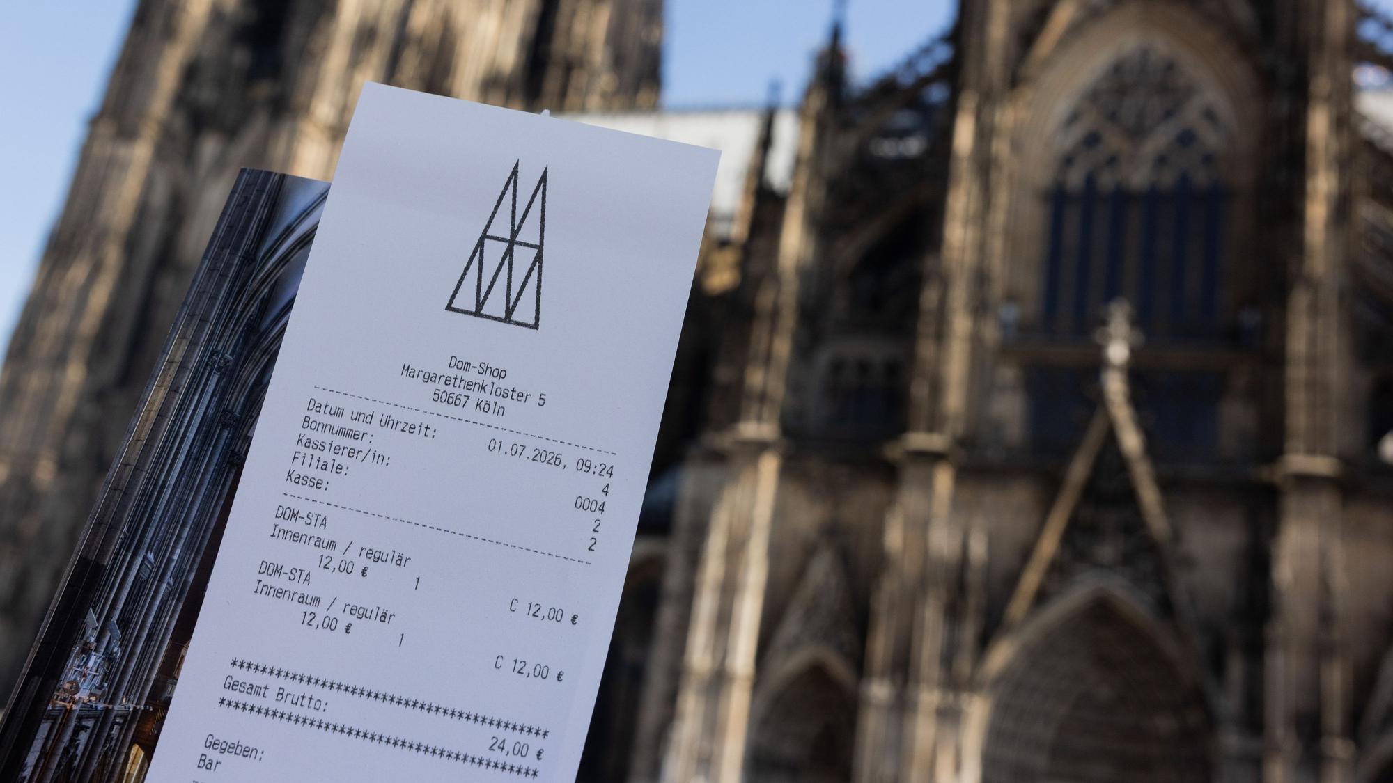 Eine Touristin zeigt ihr Ticket vor dem Kölner Dom. Der Eintritt in den Kölner Dom kostet ab dem 1. Juli zwölf Euro für Besucher. Betende sollen in einen bestimmten Bereich weiterhin kostenlos Zutritt erhalten. +++ dpa-Bildfunk +++