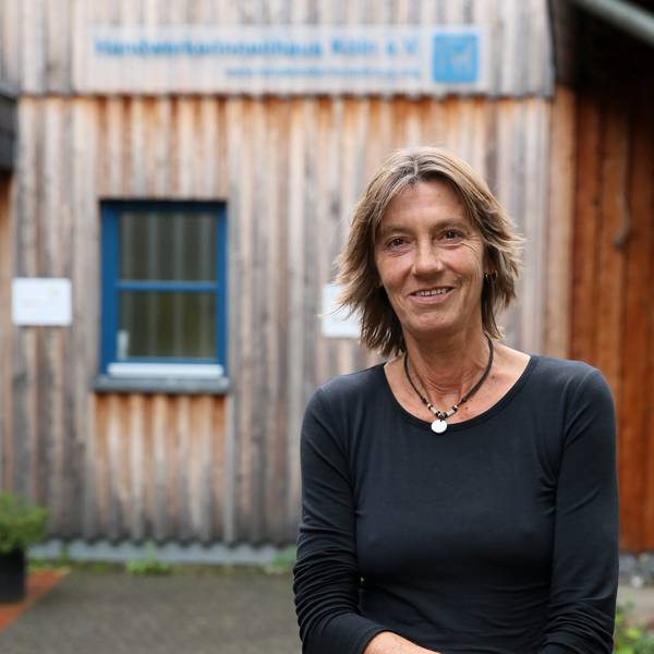 Eine Frau in Jeans und schwarzem Pullover steht vor einem Gebäude aus Holz.