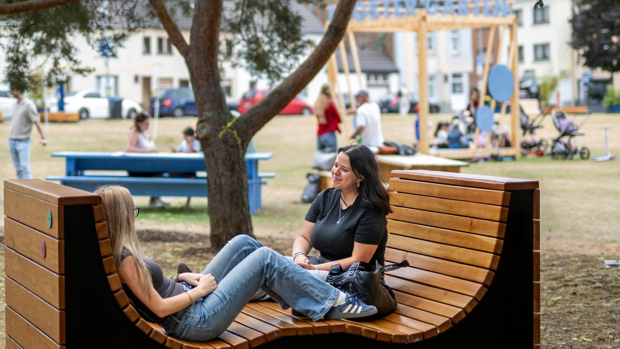 Das Bild zeigt zwei junge Frauen, die in einem wellenförmigen Sitzmöbel Platz genommen haben.
