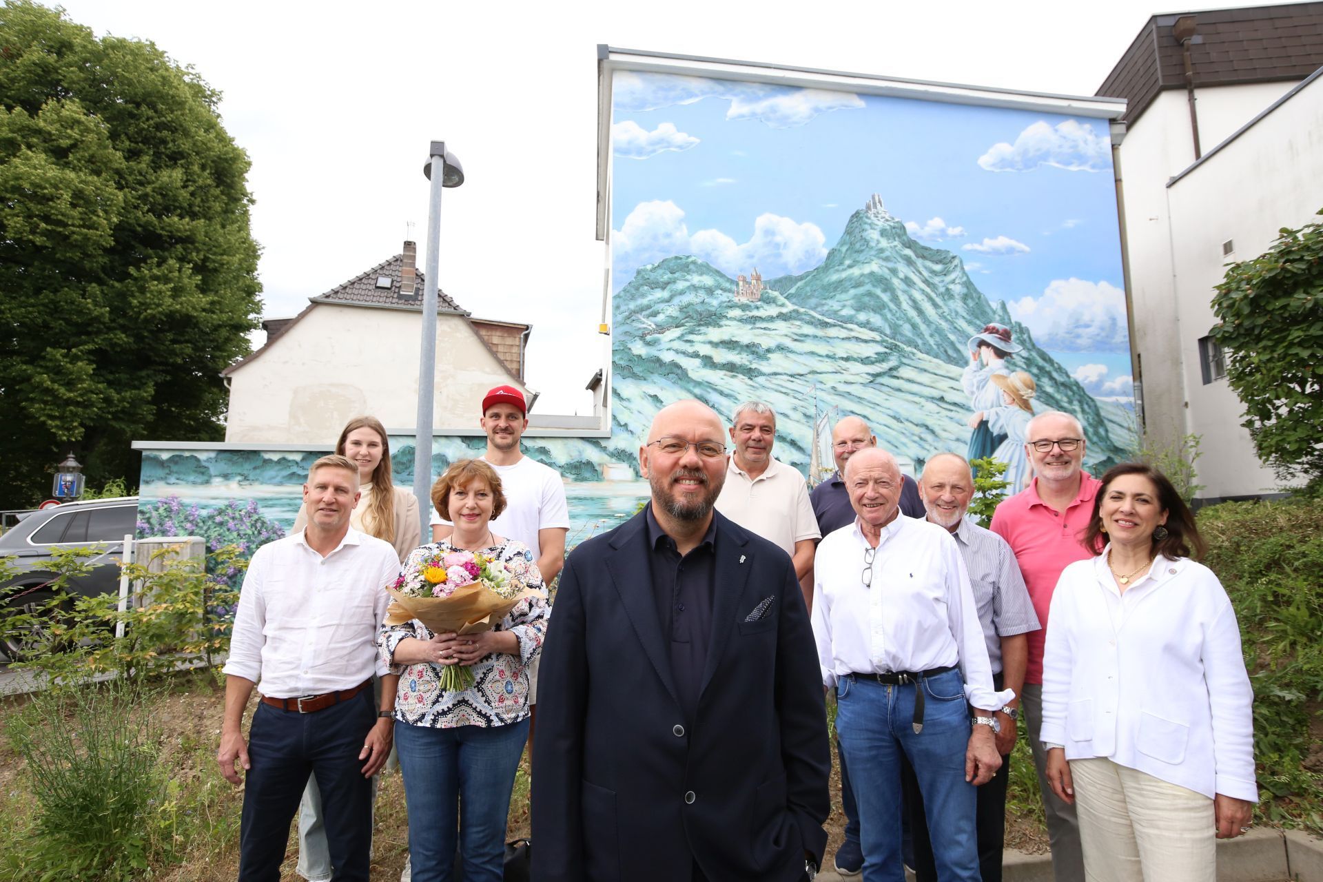 Eine Gruppe von Männern und Frauen vor einem großen Bild auf einer Hausfassade.