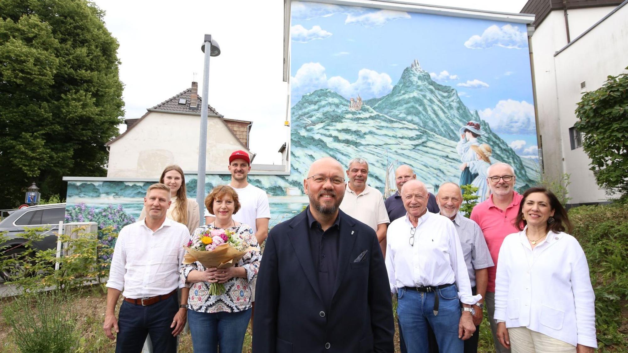Eine Gruppe von Männern und Frauen vor einem großen Bild auf einer Hausfassade.