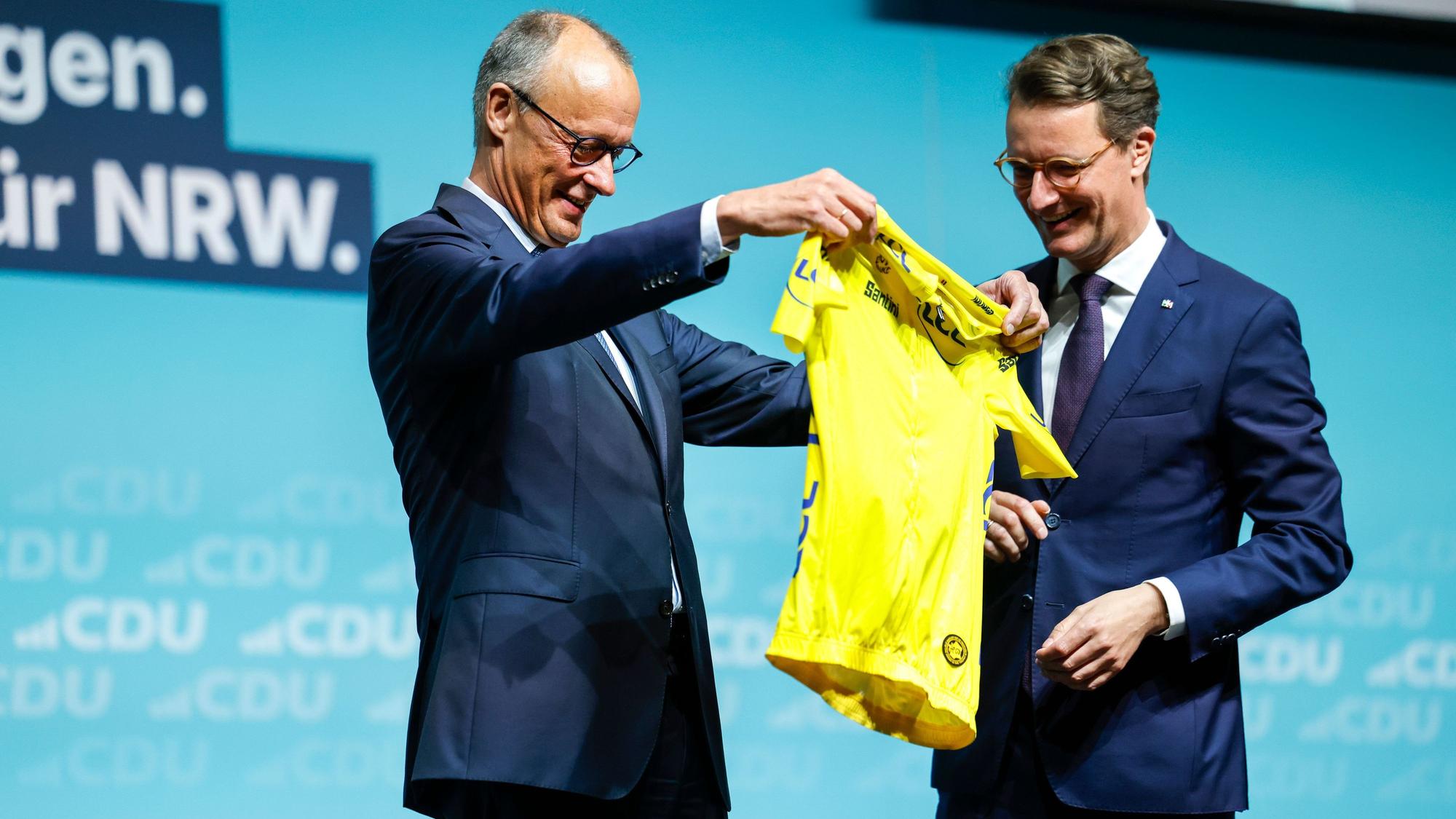 Hendrik Wüst (r,CDU), Ministerpräsident von Nordrhein-Westfalen, überreicht Bundeskanzler Friedrich Merz (CDU) beim Landesparteitag der CDU Nordrhein-Westfalen ein gelbes Rennradtrikot, dies ist das prestigeträchtigste Symbol bei der Tour de France. Es kennzeichnet den Führenden in der Gesamtwertung.